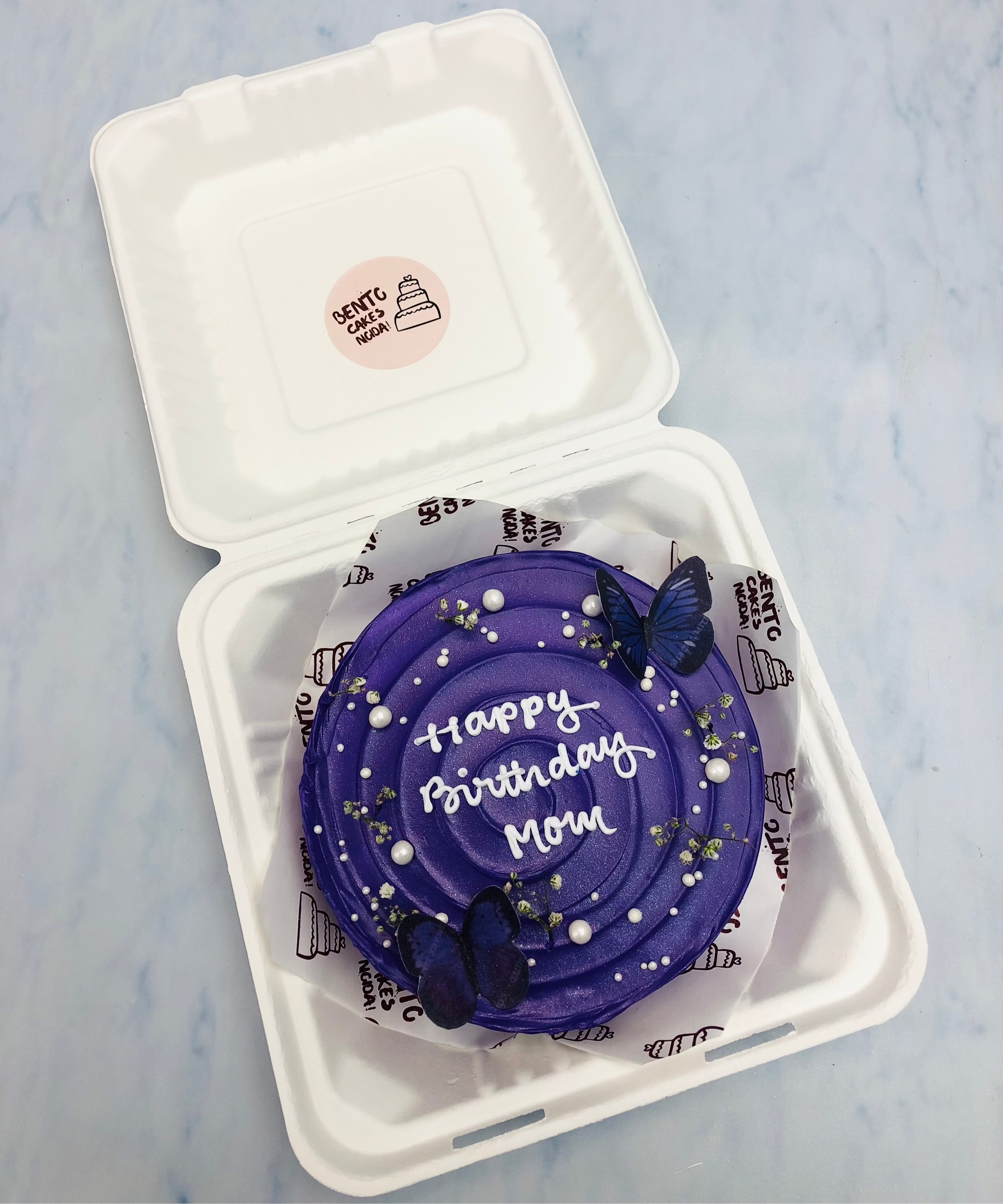 A dark blue frosting bento cake decorated with blue butterflies and aesthetic floras for Moms birthday.