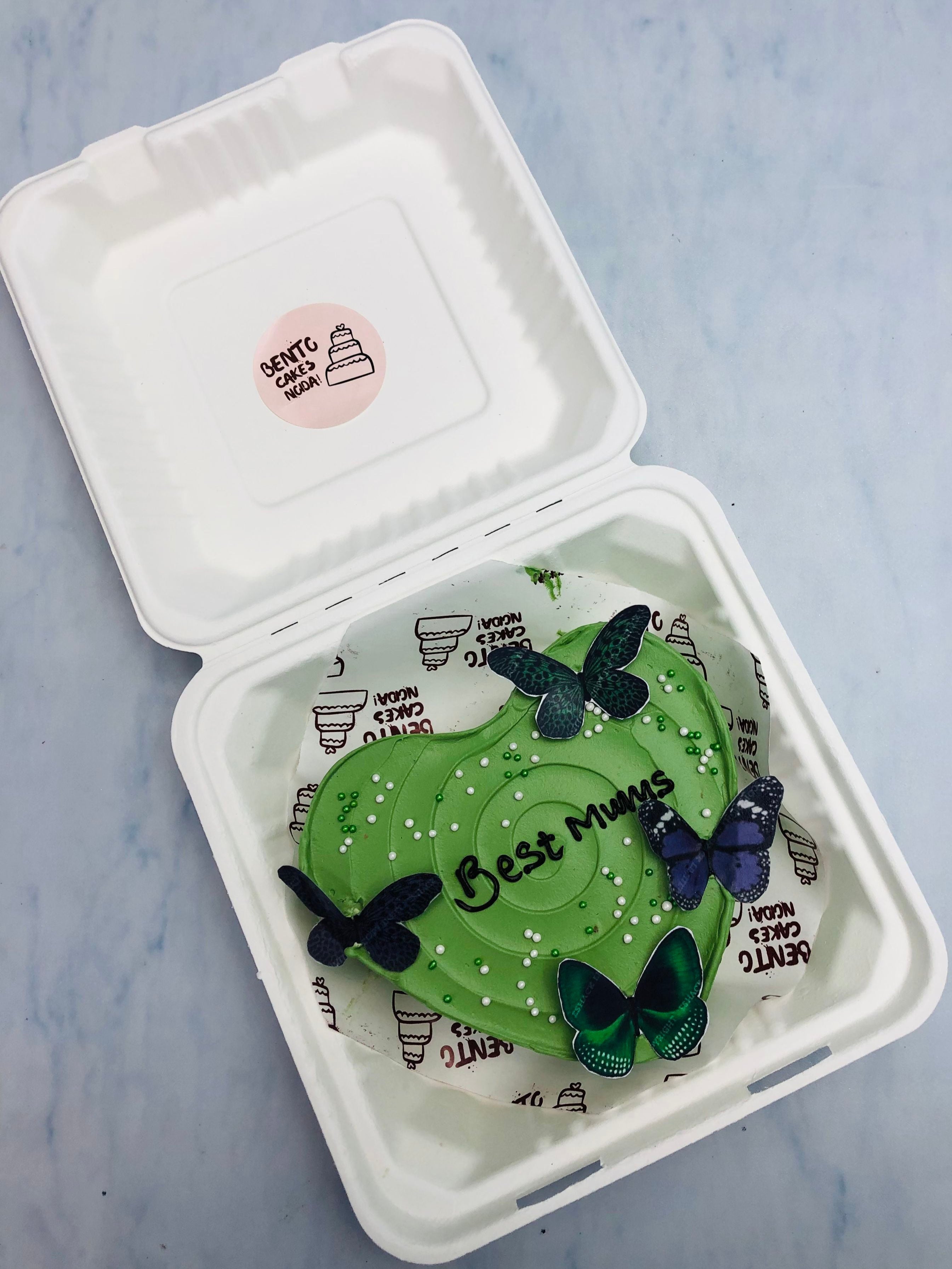 A dark green heart shape cake with blue gtreen butterflies on top.