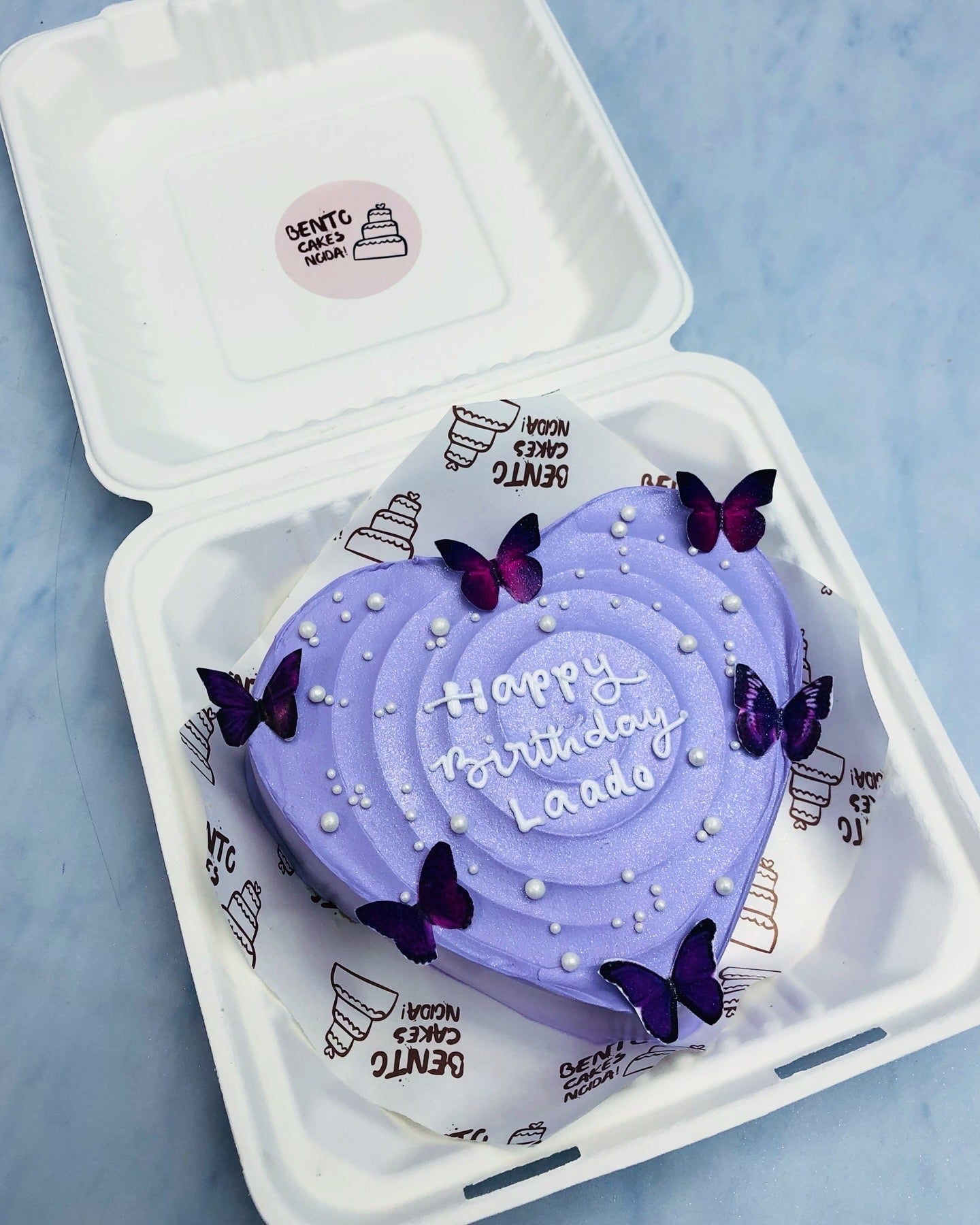 A purple color heart shape cake with purple butterflies on it's surrounding.