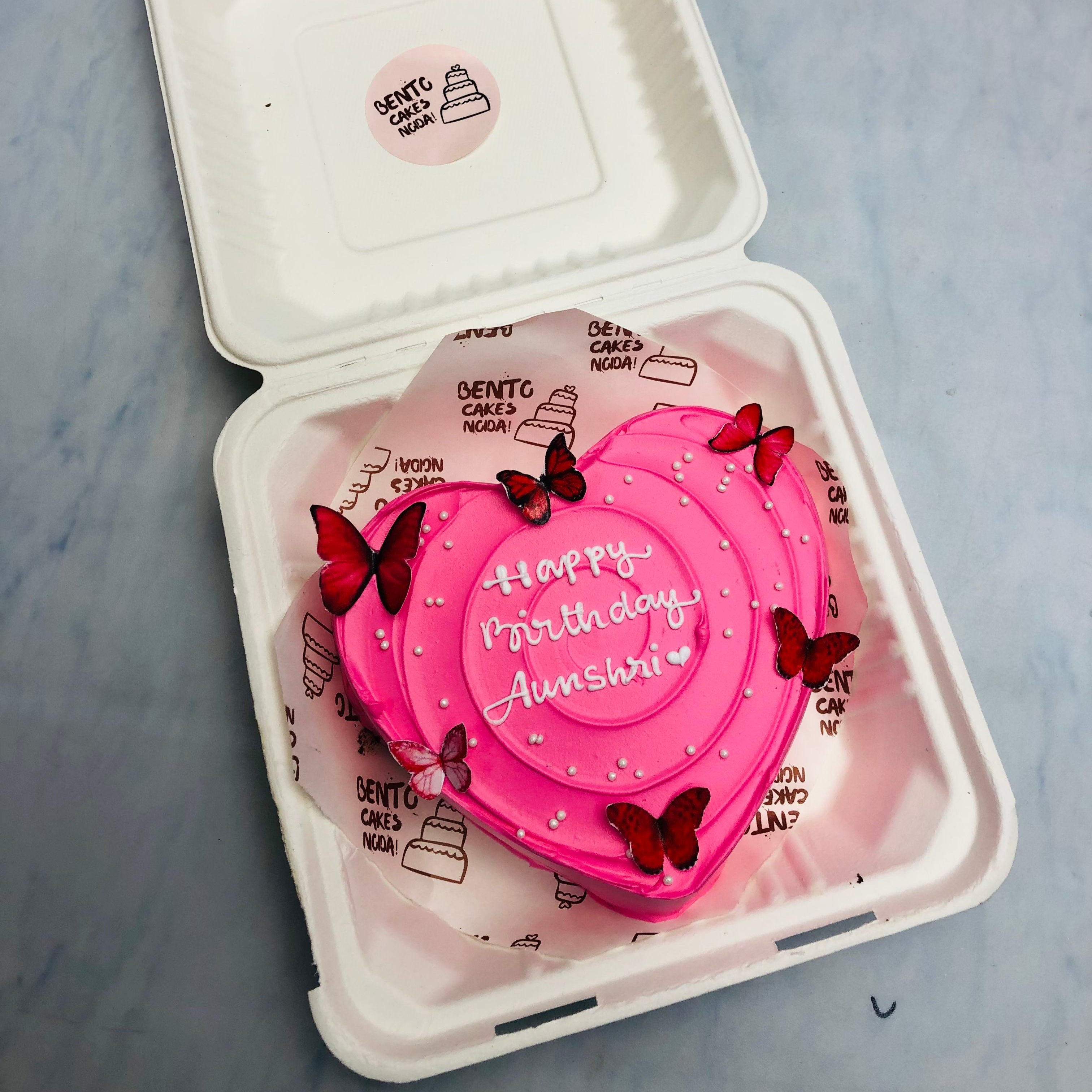 A cool pink color heart shape cake with red butterflies on its boundary.