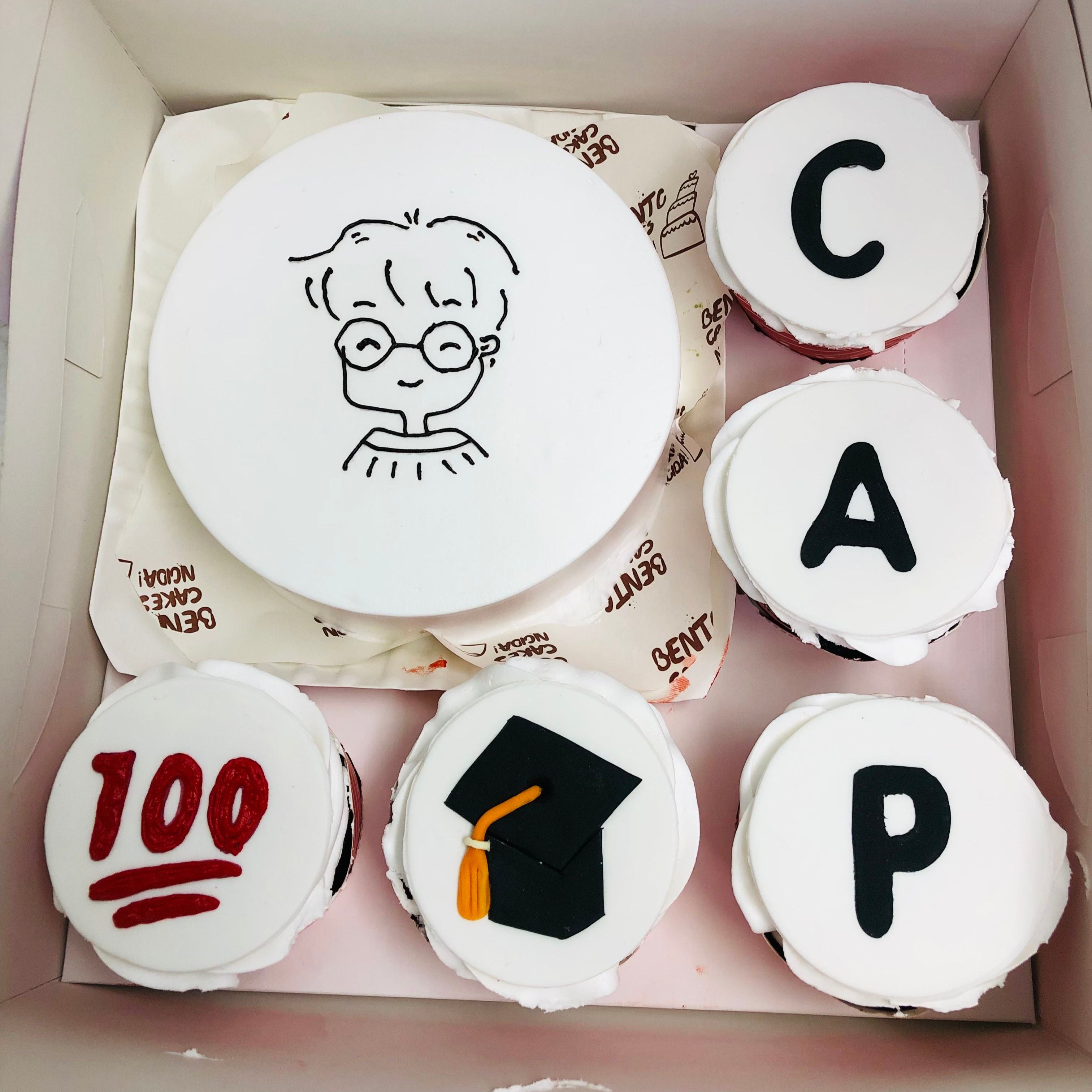 A delightful assortment of cupcakes in a box, featuring the words "cap" and "graduation" to mark a special occasion.