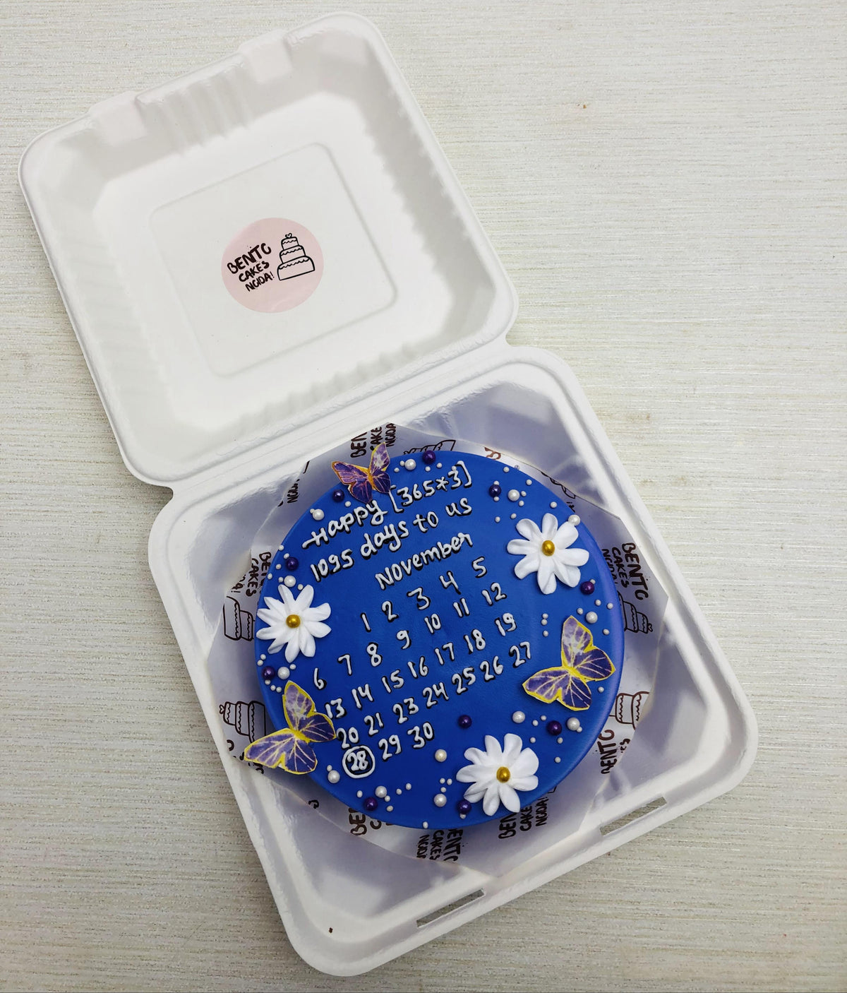 A dark blue calendar theme bento cake having florat and butterflies decoration.
