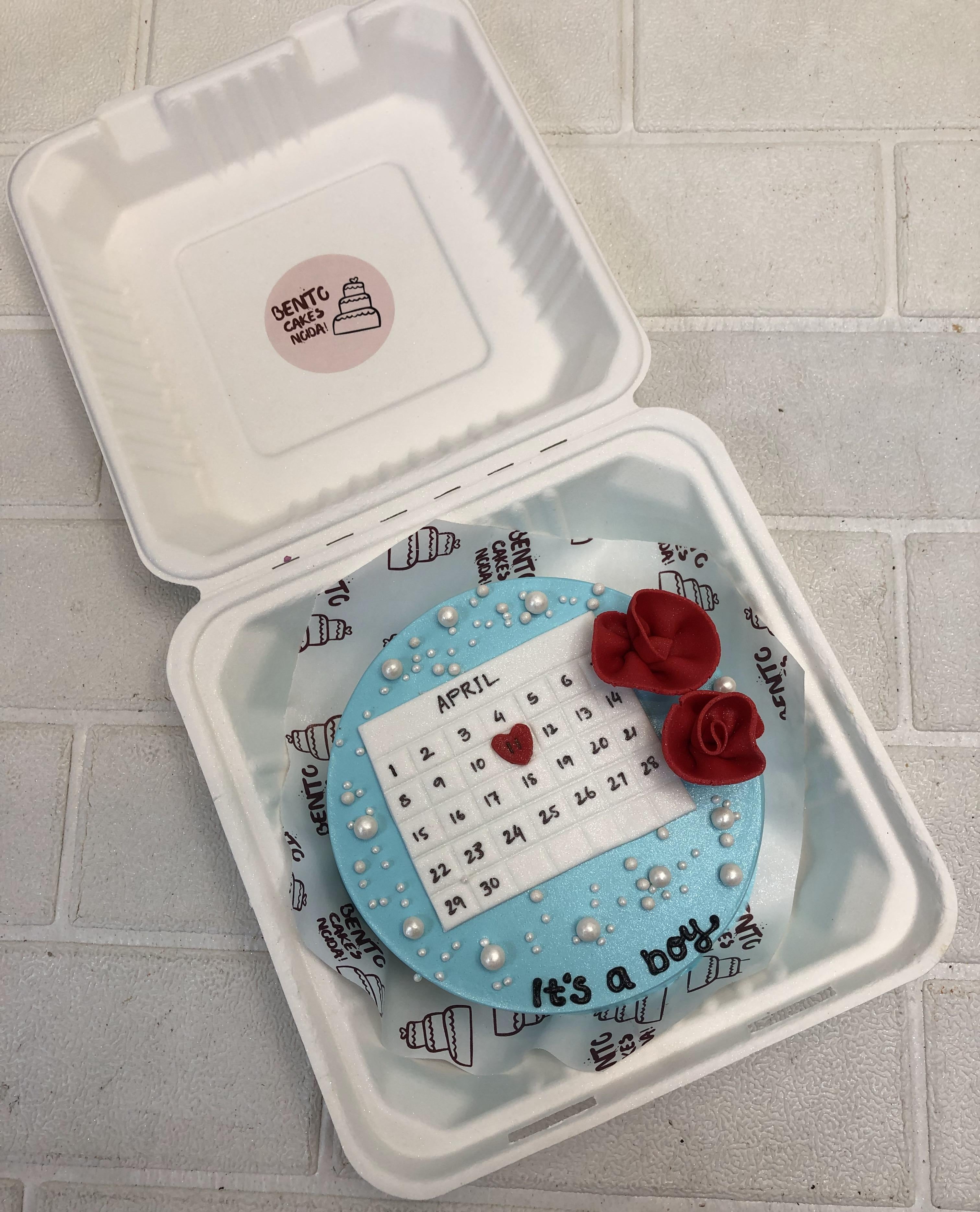 A shiny skyblue bento cake with with findant calendar design and decorated with fondant red roses and white sprinkles.
