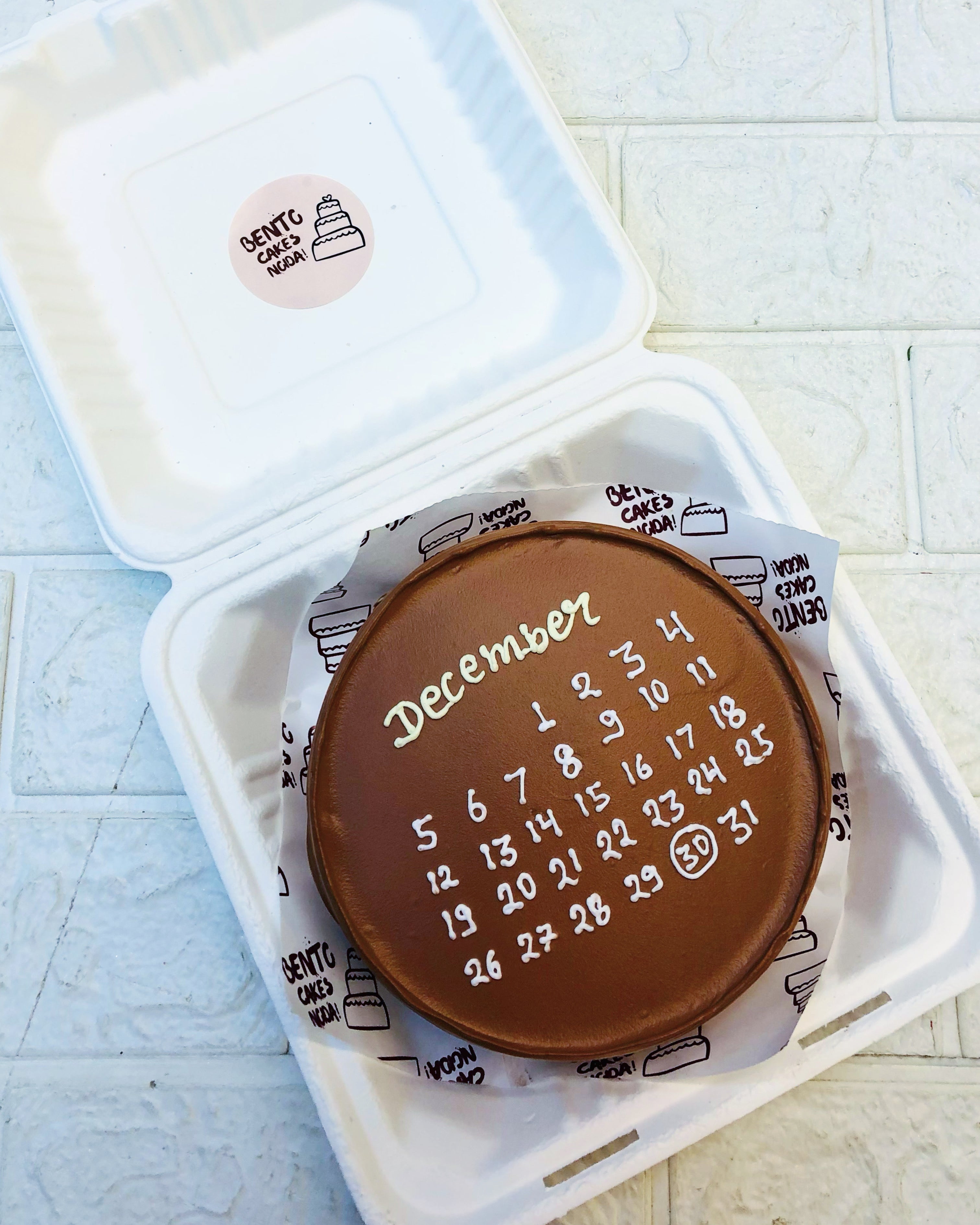 A chocolaty brown bento cake with white calendar design on it.