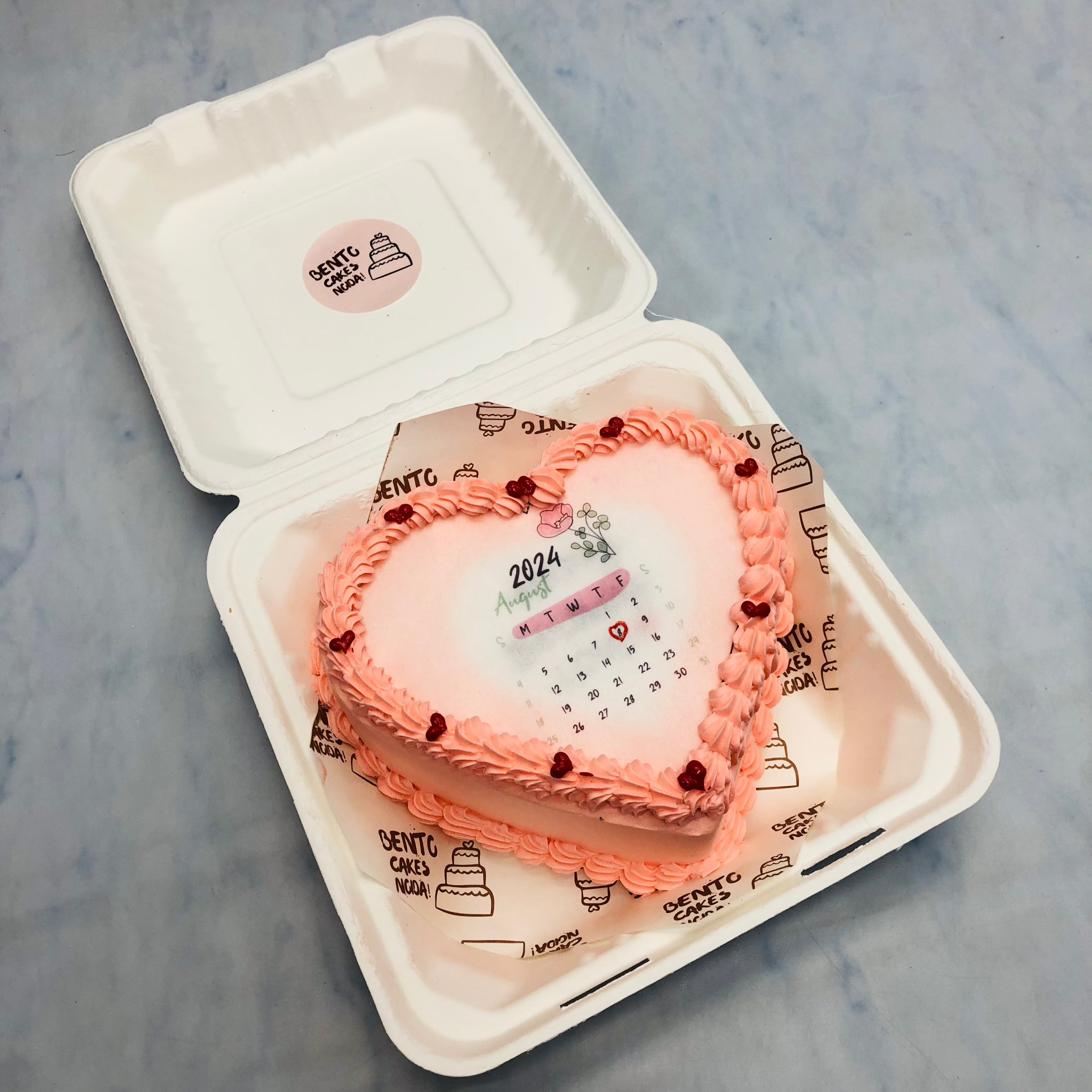A heart shape rose pink fire bento cake with calendar design on it.