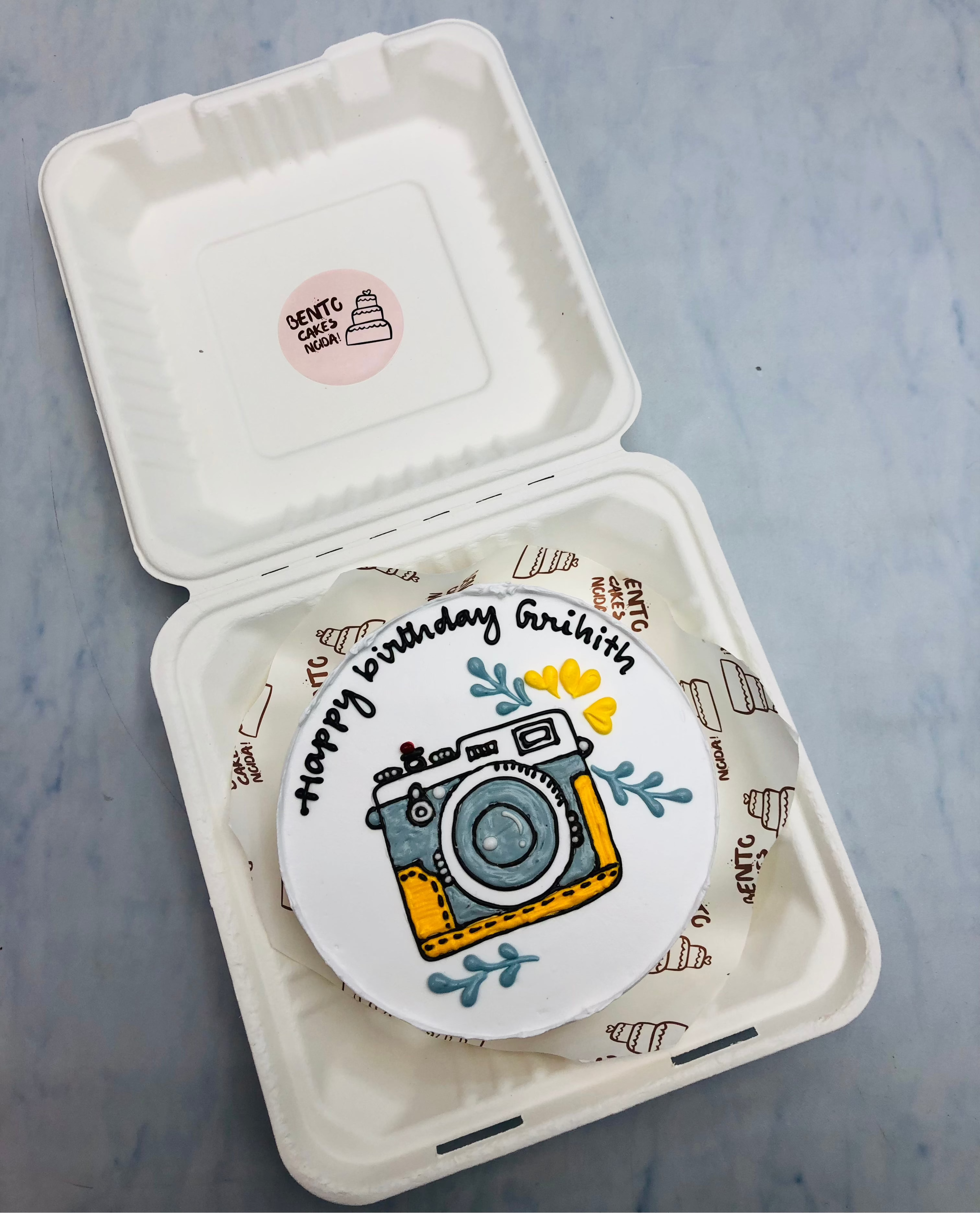 A beautiful camera design on white bento cake having floral design on it.