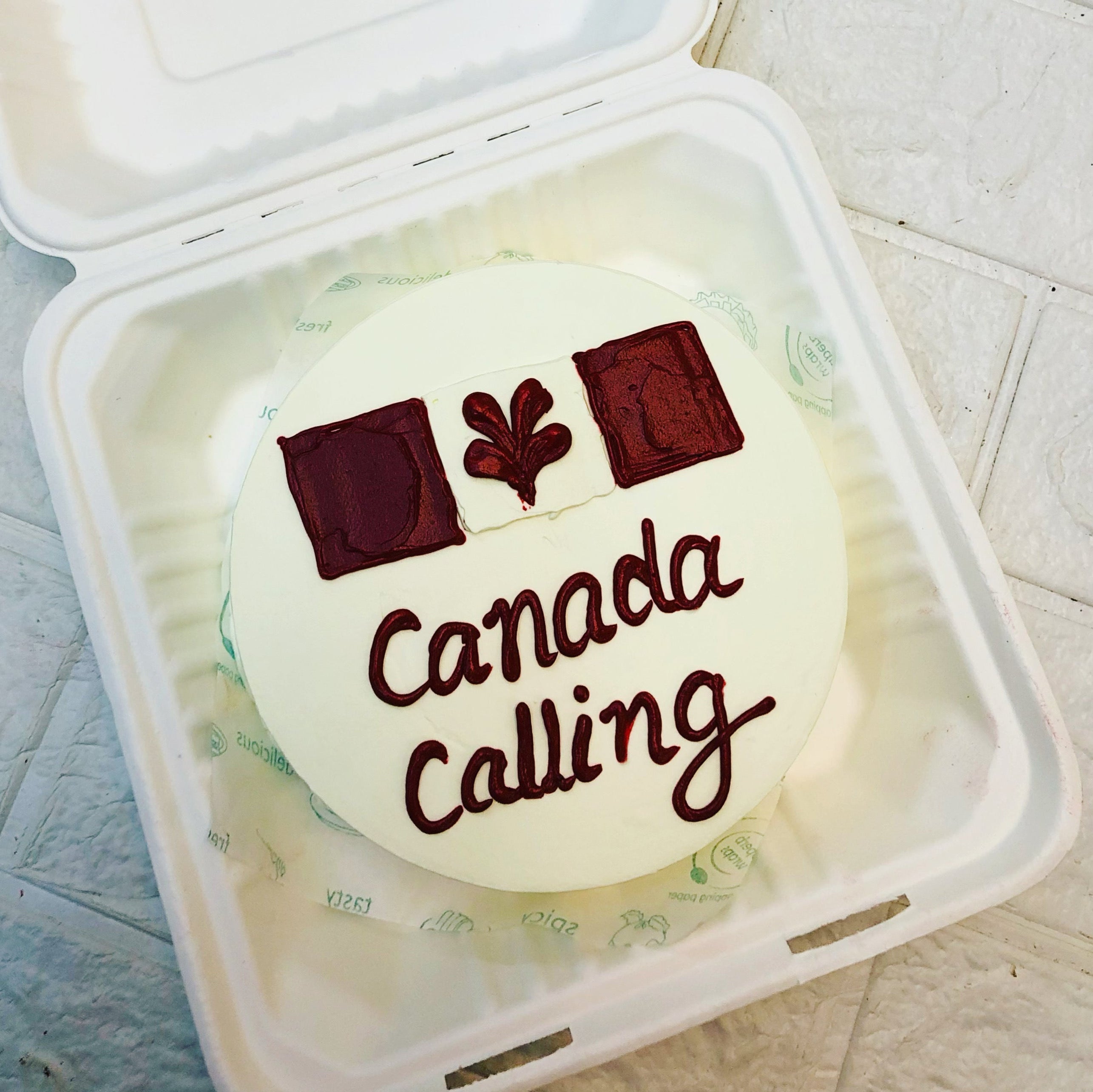 A Canadian flag cake in a box, adorned with the phrase "Canada Calling," celebrating national pride and festivities.