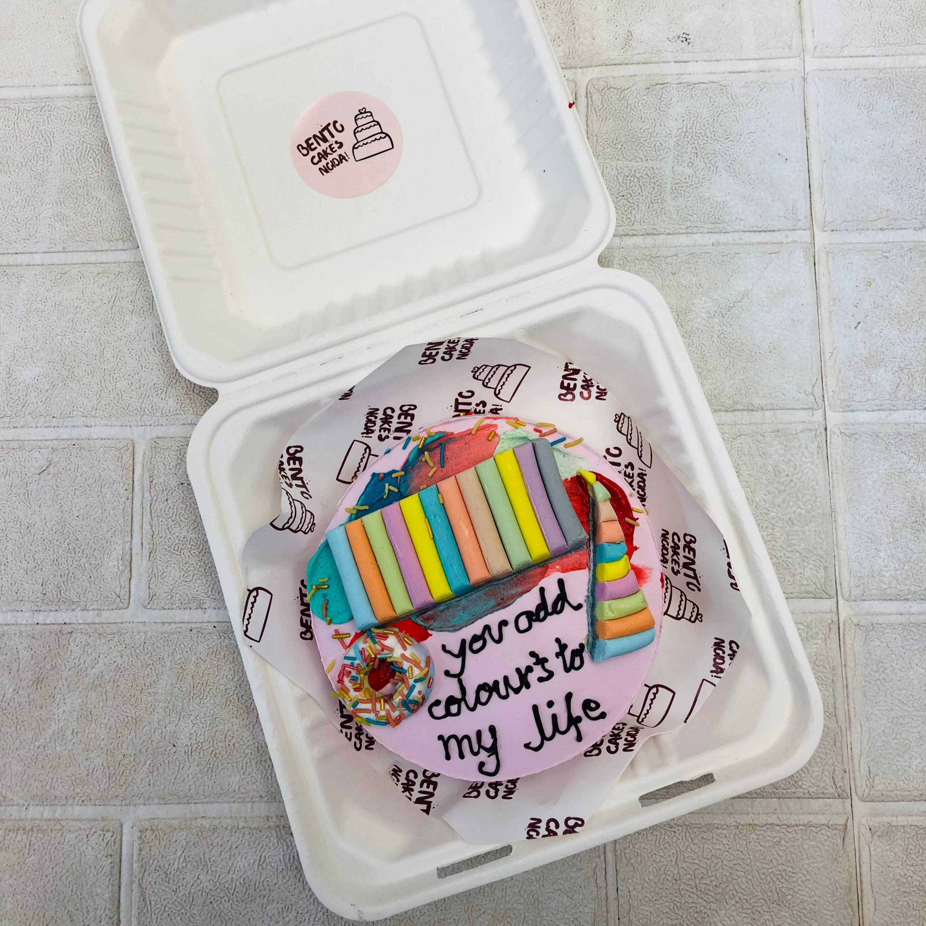 A light purple cake decorated with color designs and donut design paced on cake.