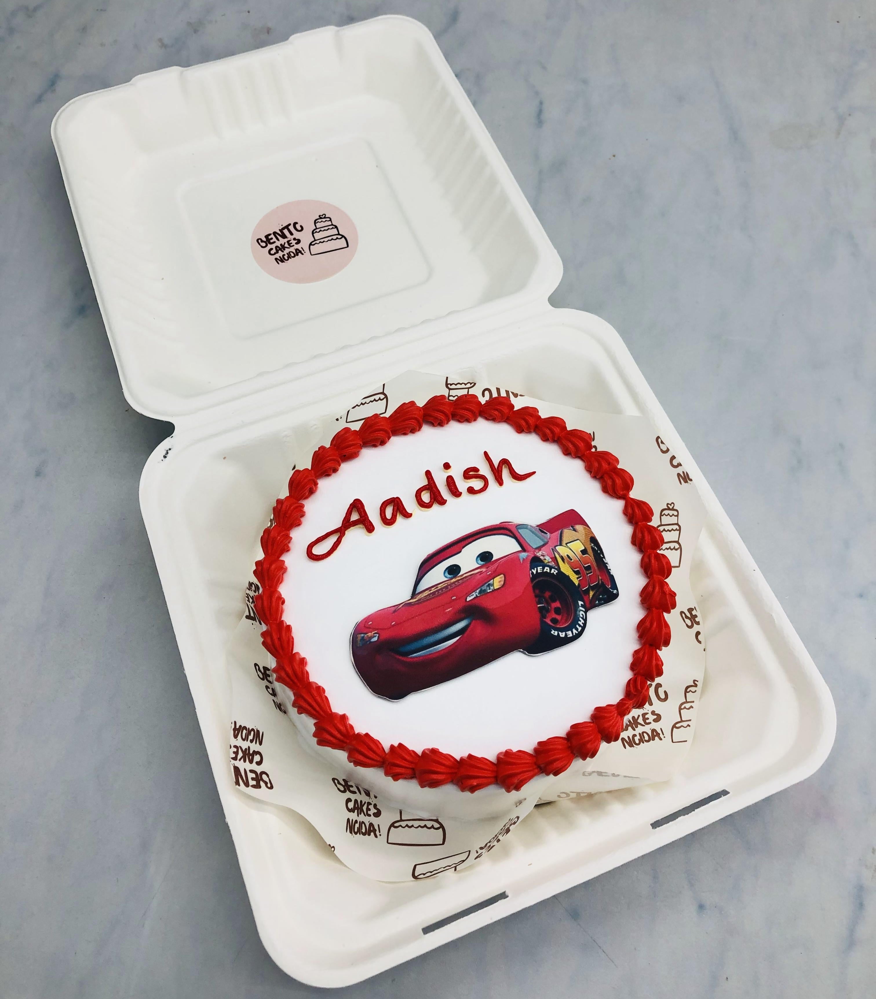 A white bento cake with a McQueen car cartoon theme with red truffle design on border.