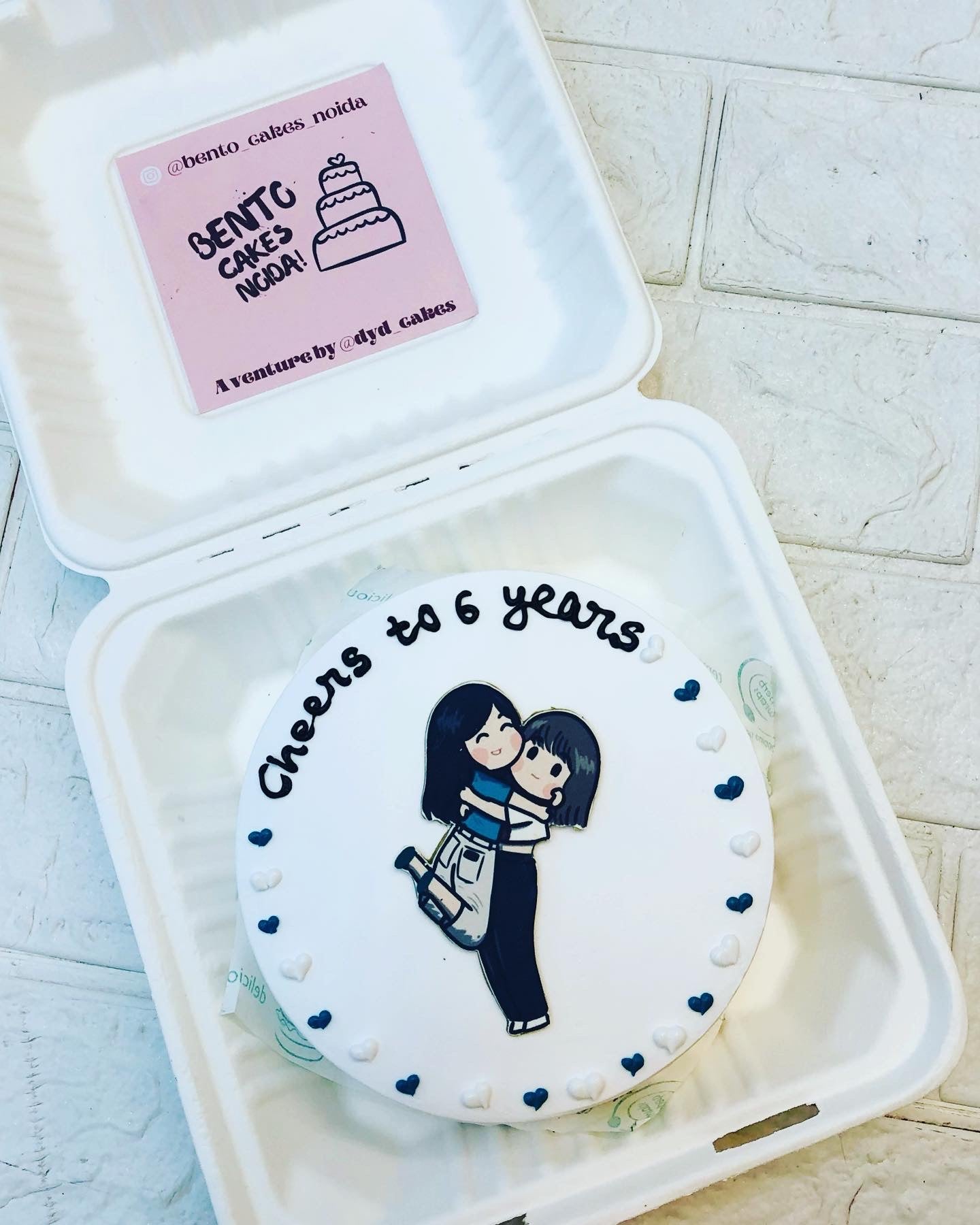 A whimsical cake featuring a cartoon girl hanging another girl, beautifully presented in a decorative box.