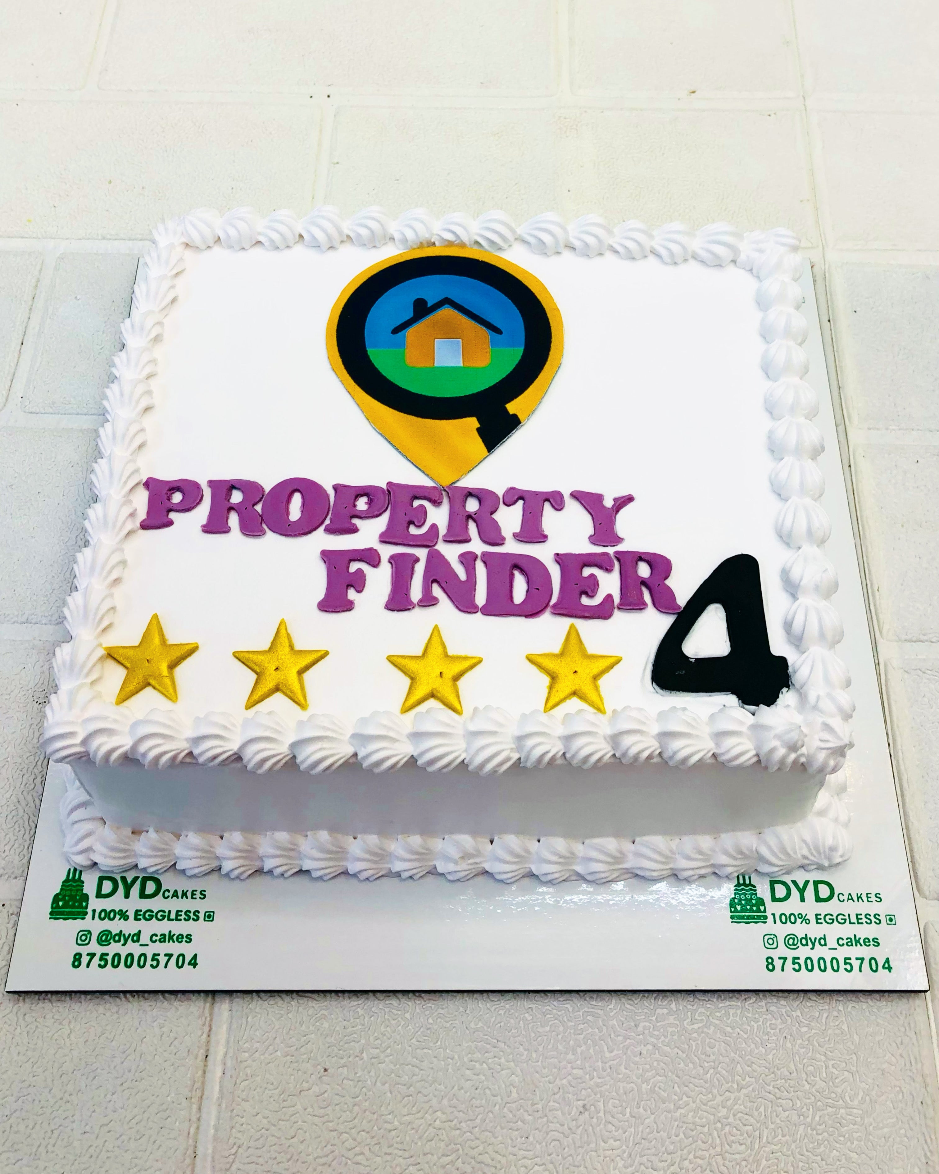 A rectangular cake with white icing, featuring the text "PROPERTY FINDER" in bold purple letters, a logo with a house inside a magnifying glass, four gold stars, and the number 4.