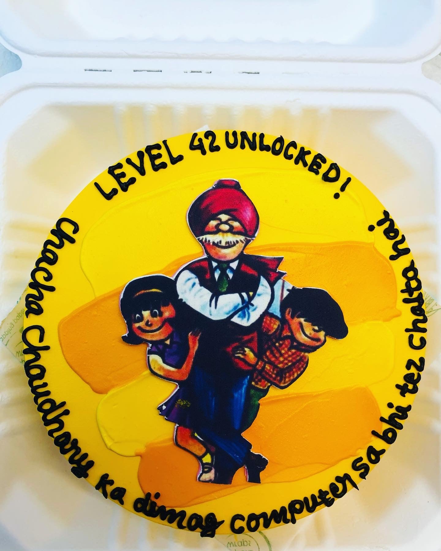 A yellow cake in a bento box created with a chacha chaudhary cartoon character on it and a text written on it.