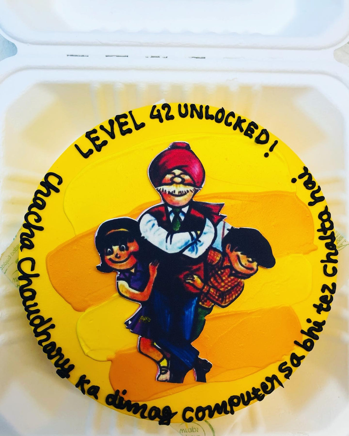 A yellow cake in a bento box created with a chacha chaudhary cartoon character on it and a text written on it.