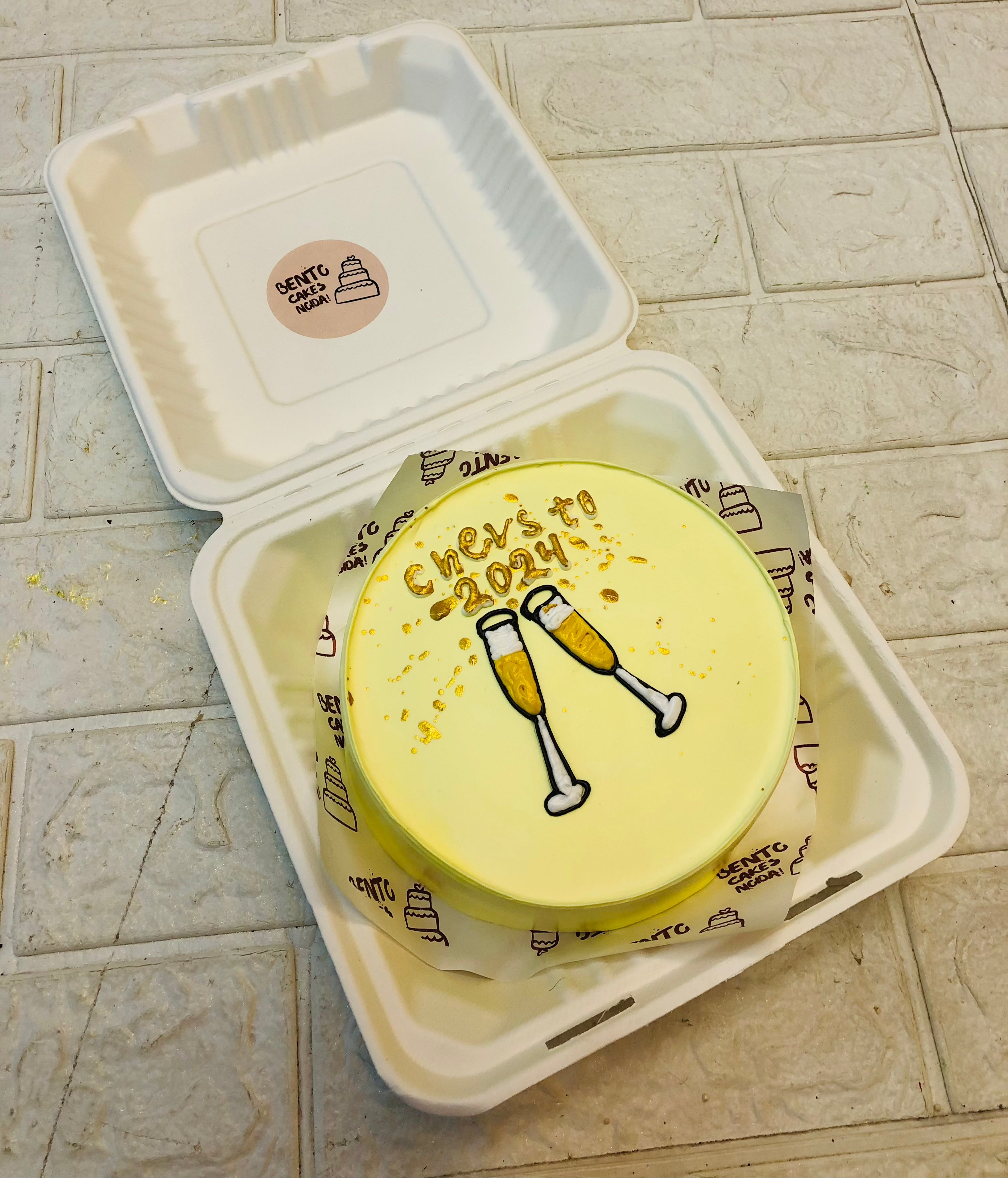 A light yellow bento cake having two cheers glass design for new year celebration.