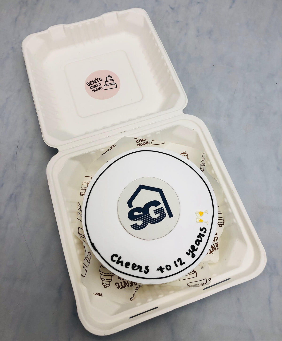 A white bento cake is designed on a commercial theme, celebrating 12 years.