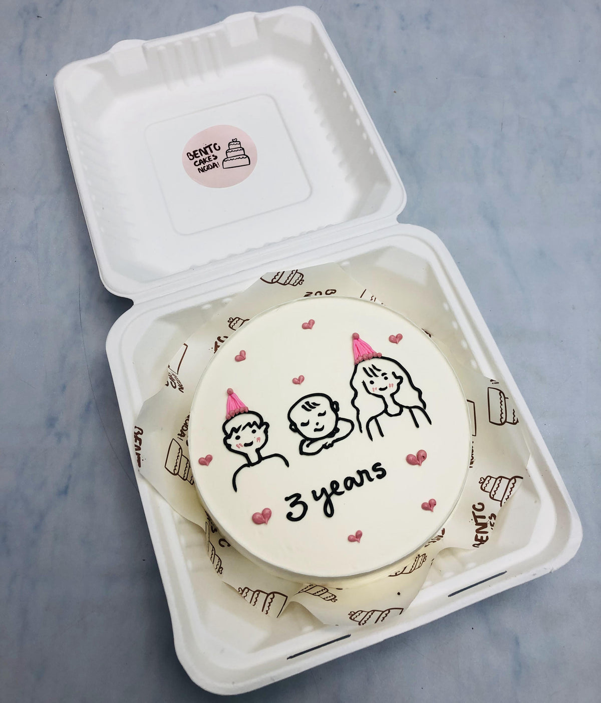 A white bento cake having a mom and ad celebrating his babies 3 years birthday.