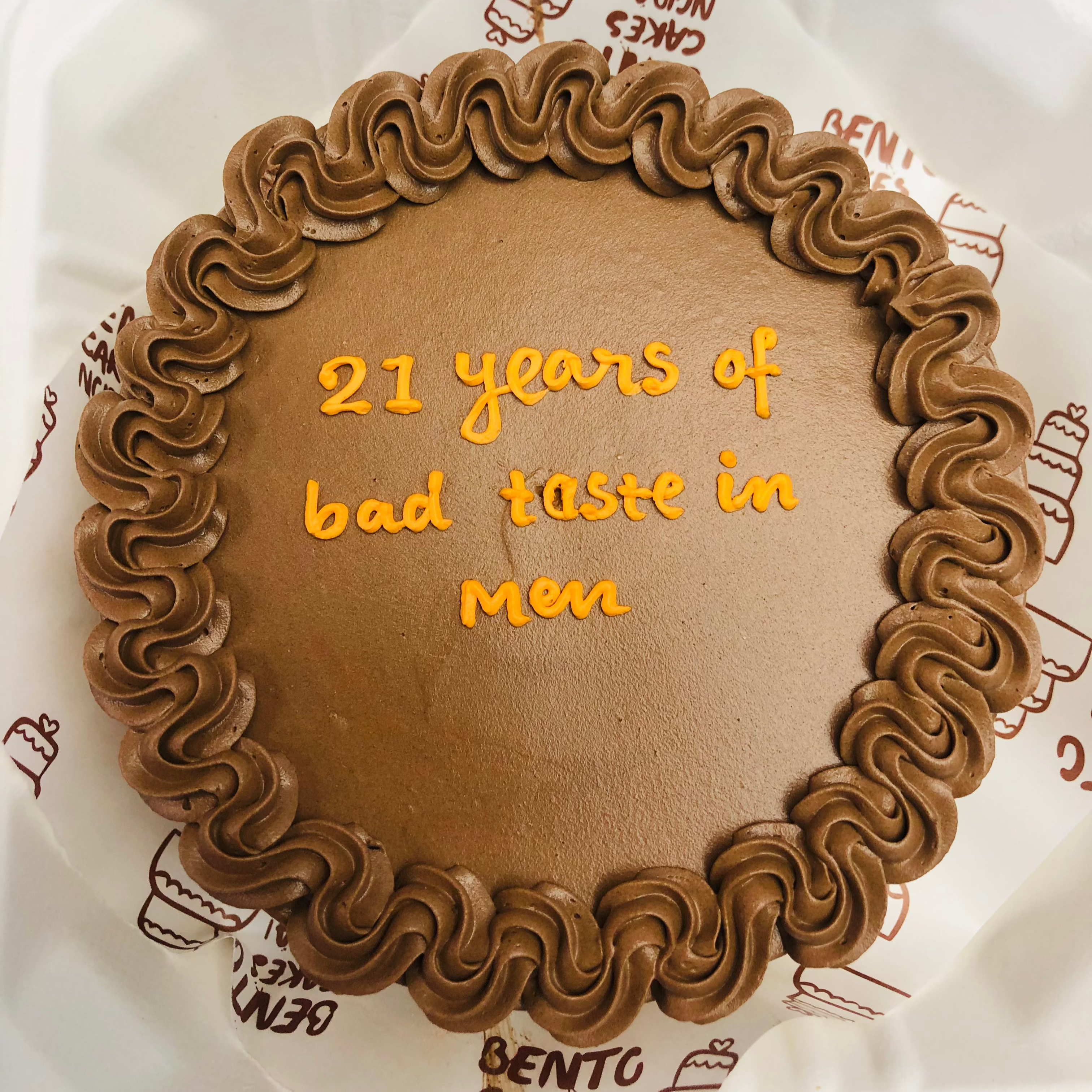 A chocolate round bento cake is designed with brown floral design on its boundary with a message on the center.