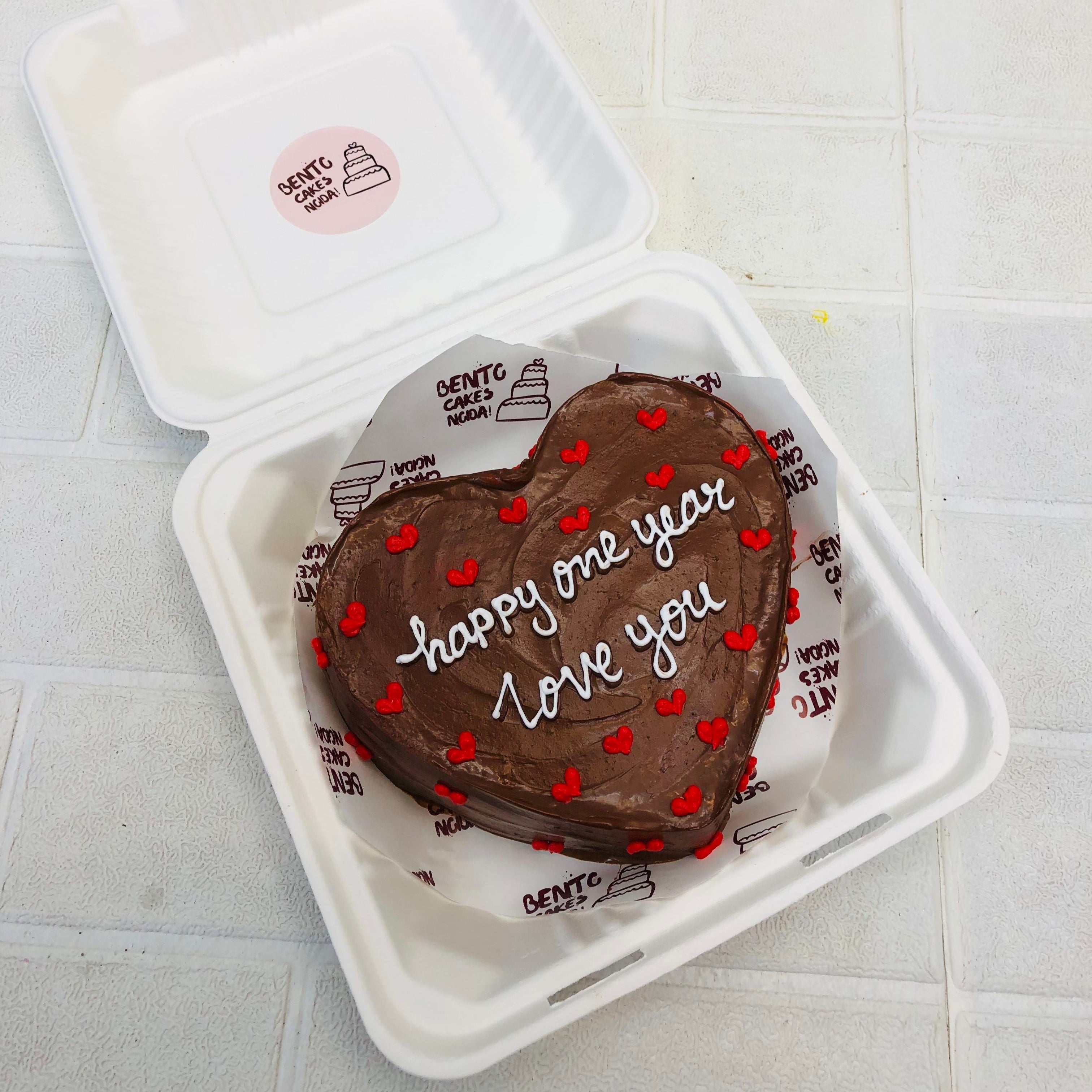 A chocolety brown heart shape cake filled with little red hearts and a loving text witten with white icing.