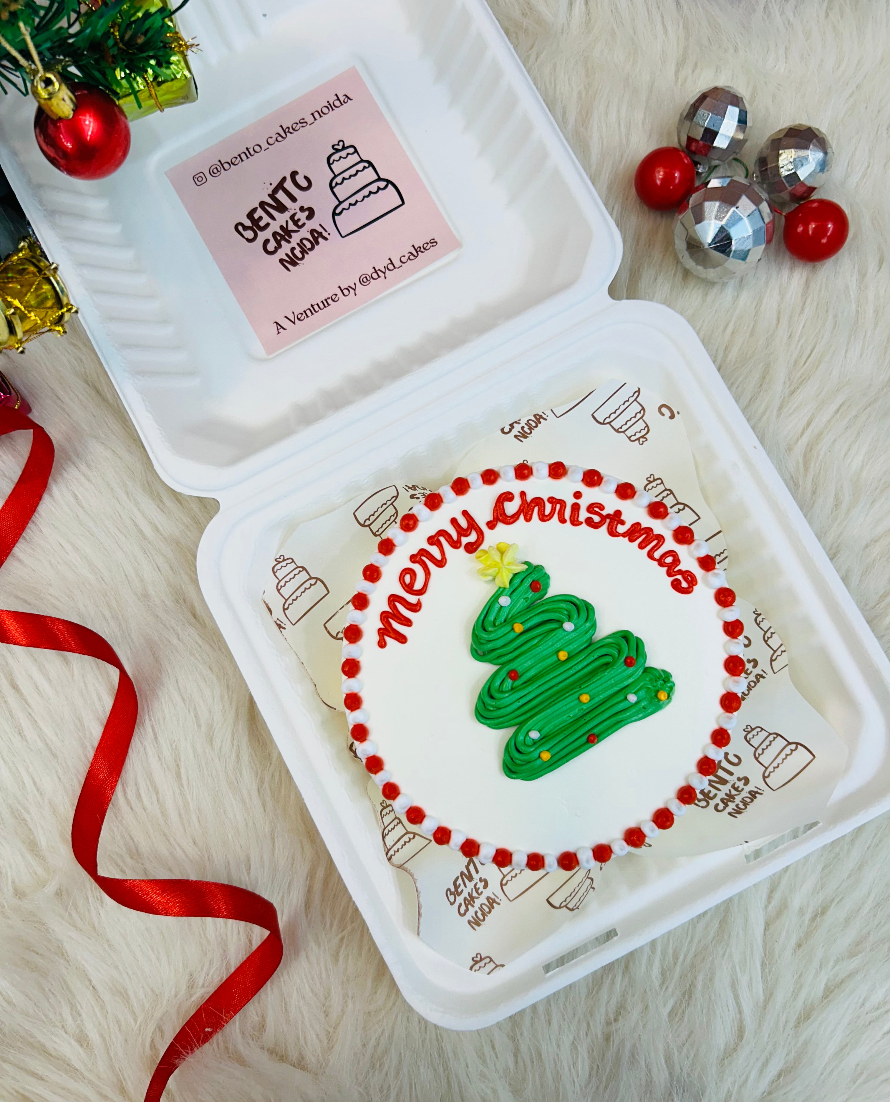 A white bento cake is designed for merry christmas with a snake type green christmas tree design on it.