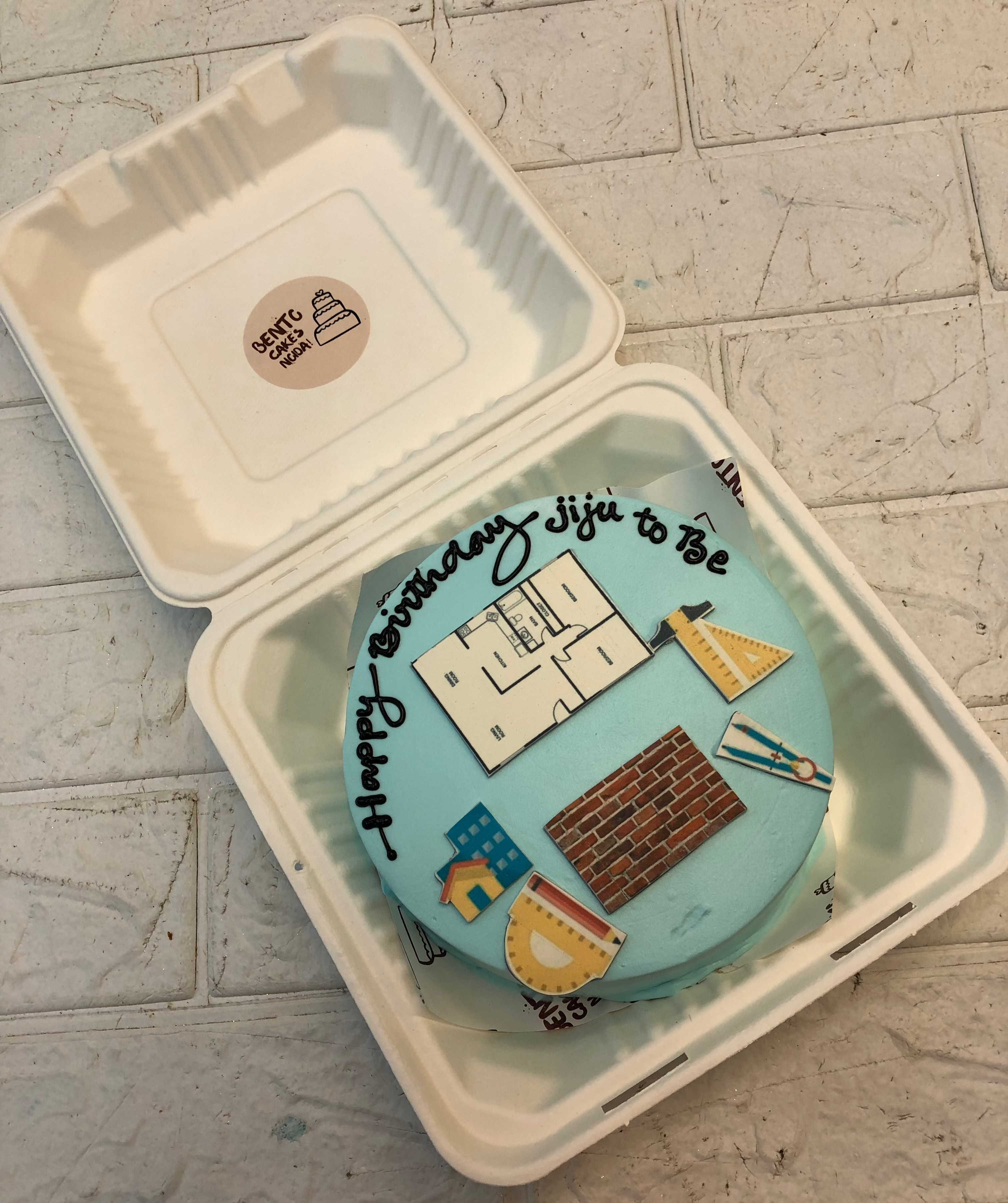 A skyblue bento cake is designed for a civil engineers birthday with engineering equipments print on it.
