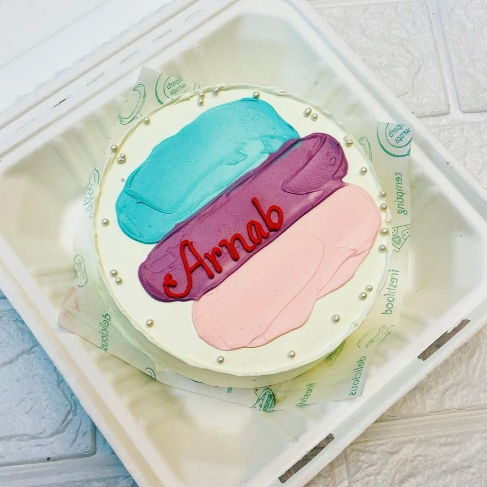 A cake displayed in a bento box with the name "Arnab" elegantly written in icing on the top.