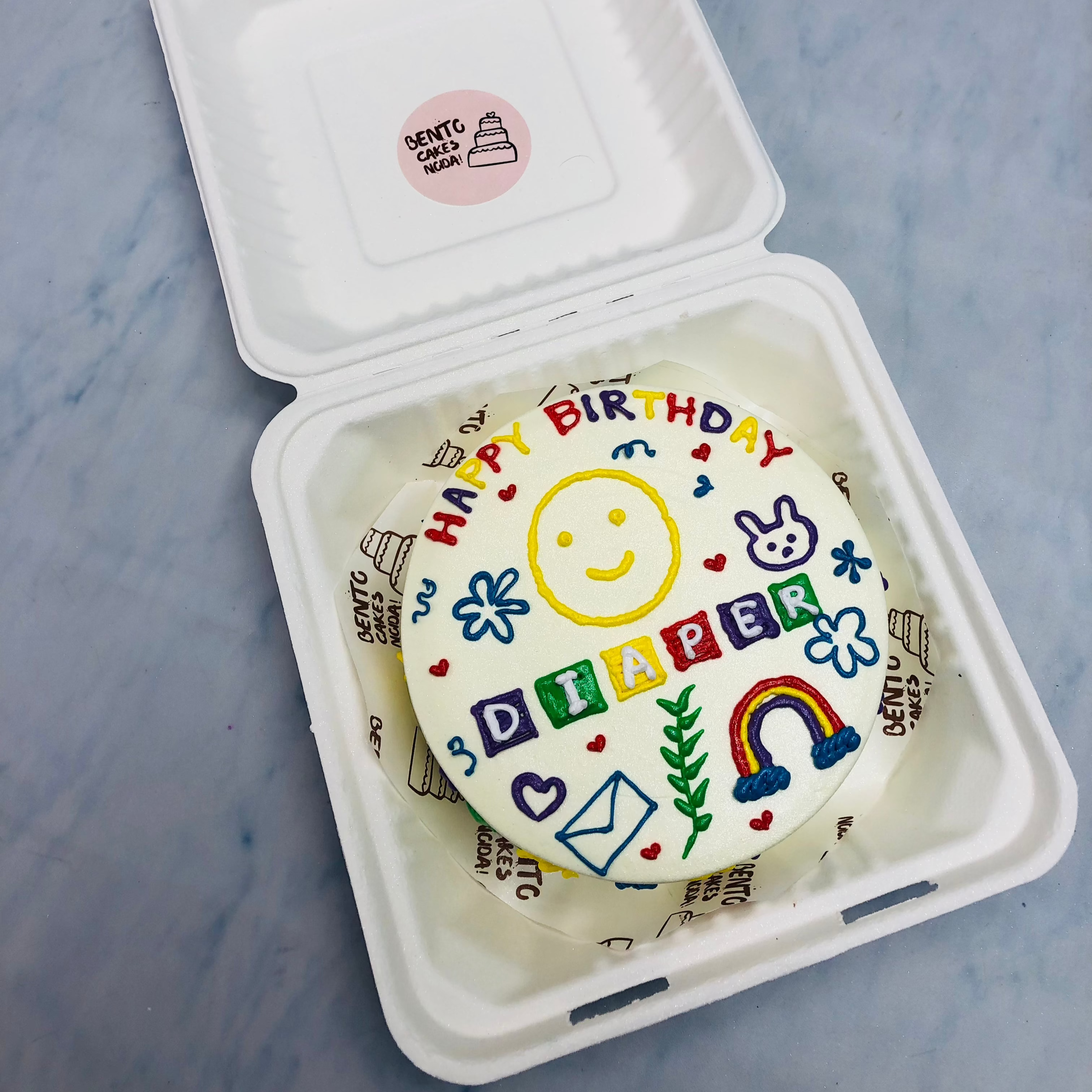 A white cake with colorful drawings and cute faces on it.