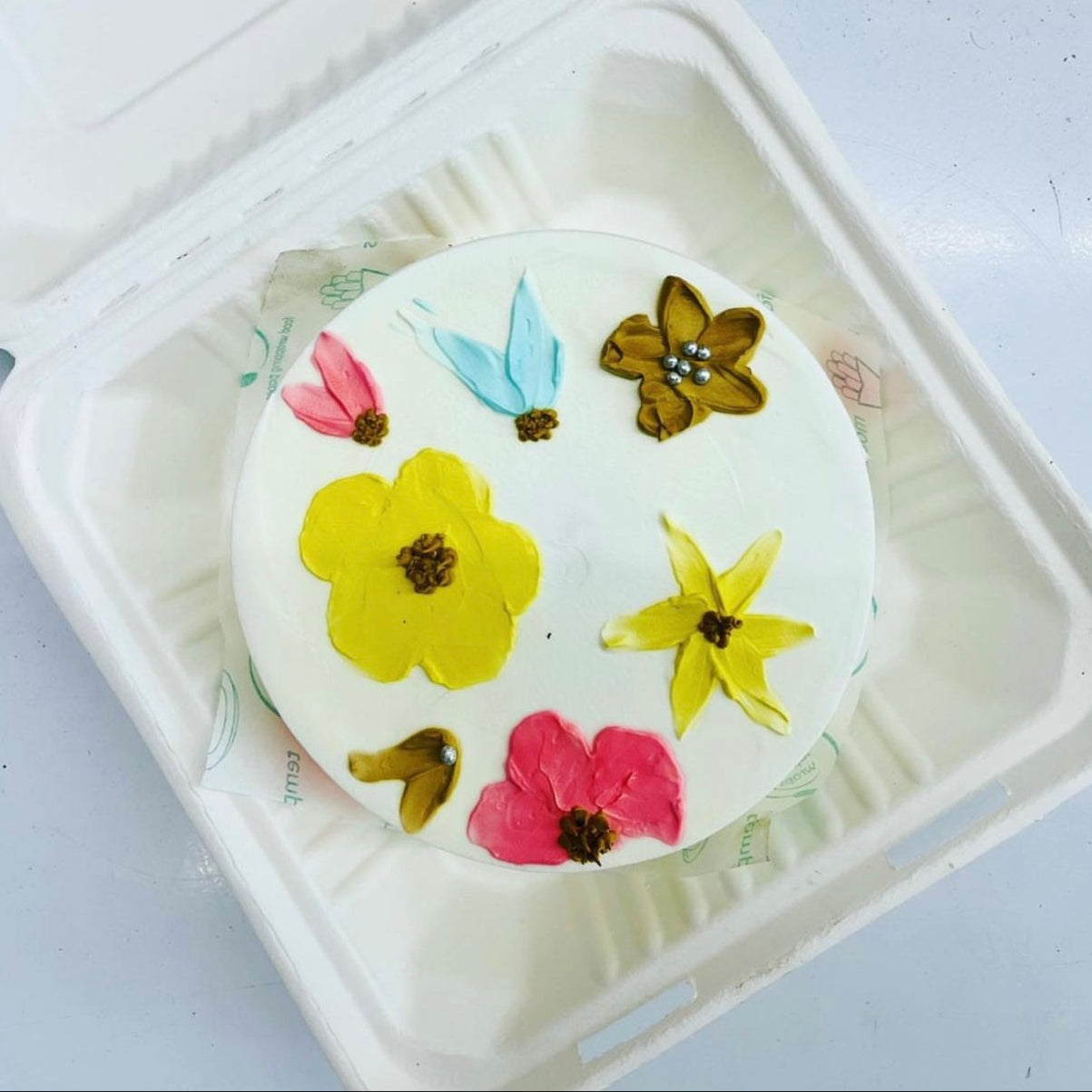 A cake displayed in a soft foam container, featuring an elegant arrangement of flowers design on its surface.