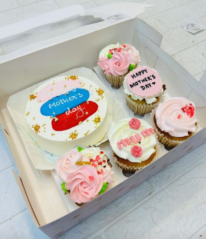 A bento box containing a cake and 5 cupcakes. Cake having colorful shades design and cupcakes having white and pink floral design.
