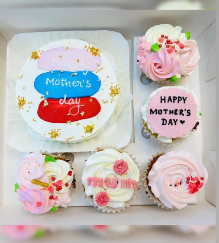 A bento box containing a cake and 5 cupcakes. Cake having colorful shades design and cupcakes having white and pink floral design.