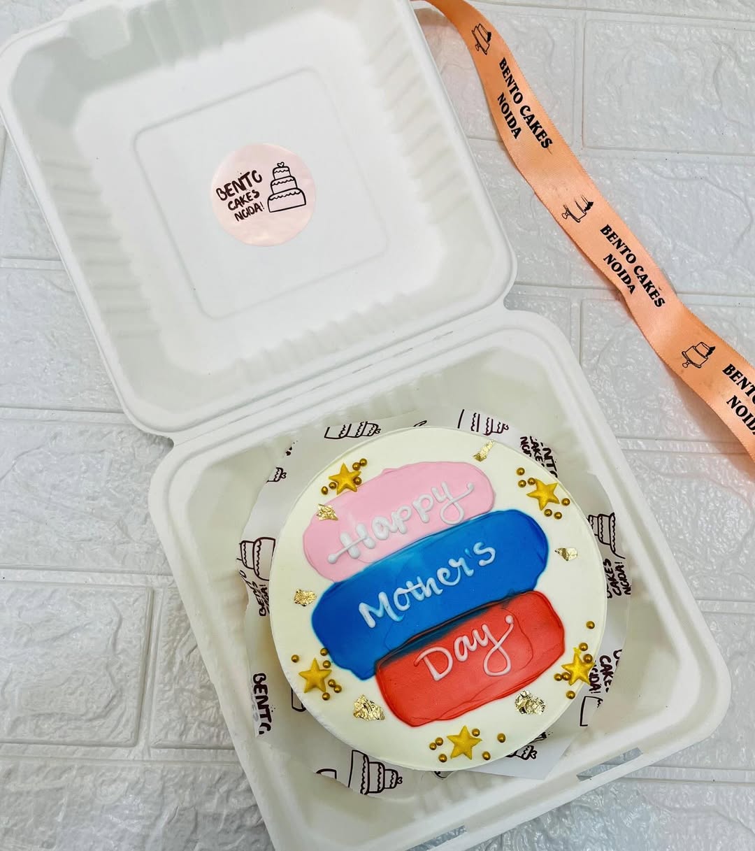 A white cake with red, blue and pink shades in the center and some golden stars and gloden foli spread all over the cake.