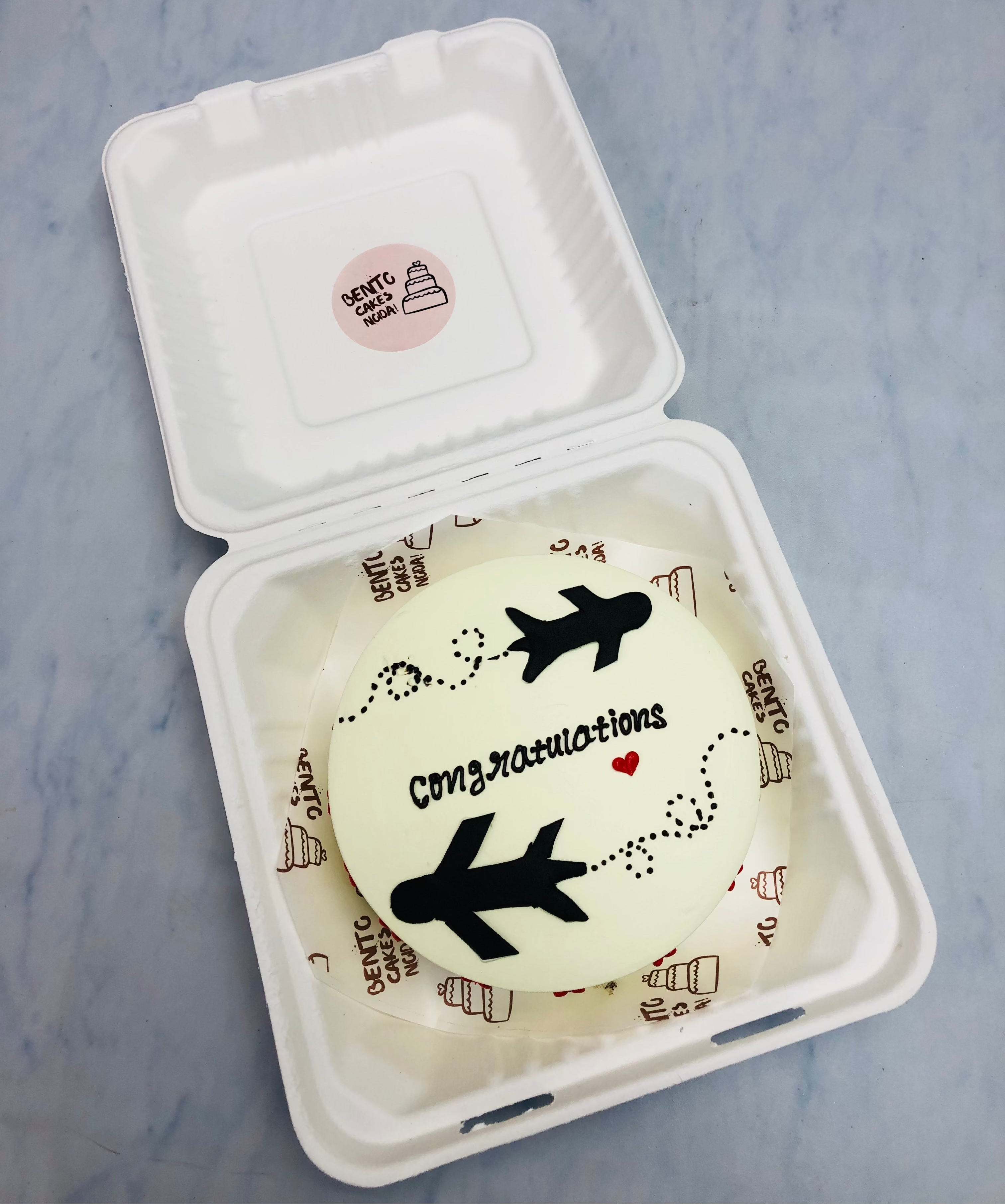 An off white bento cake having a travelling theme by flight with a congratulatons text.