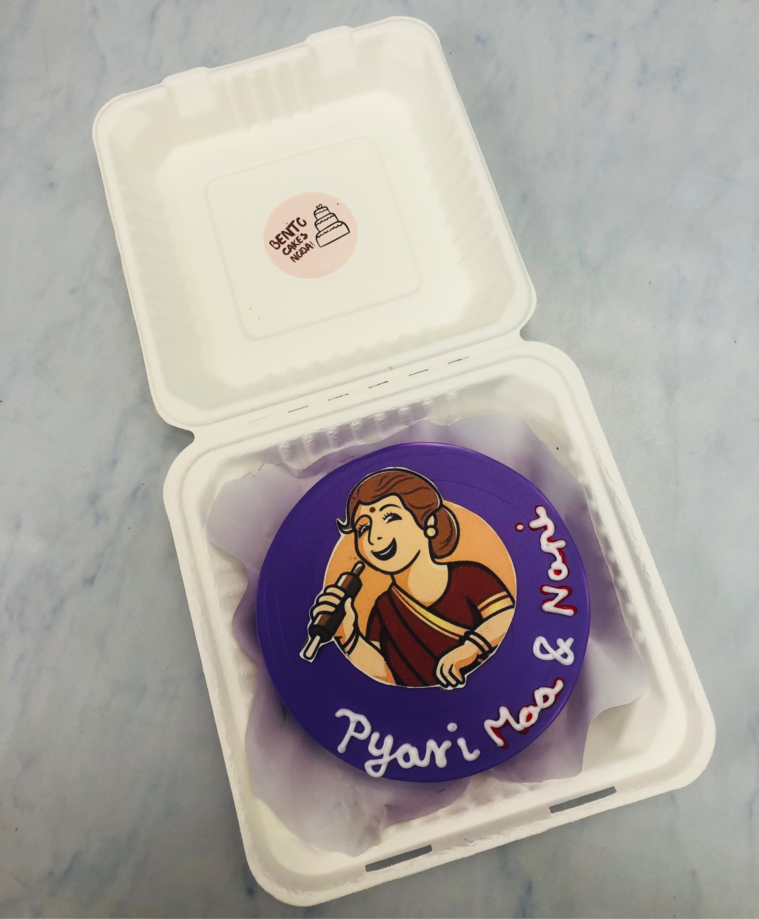 A beautifully decorated purple cake featuring an illustration of a woman in a red saree holding a microphone, with the words "Pyari Maa & Nani" written in white.