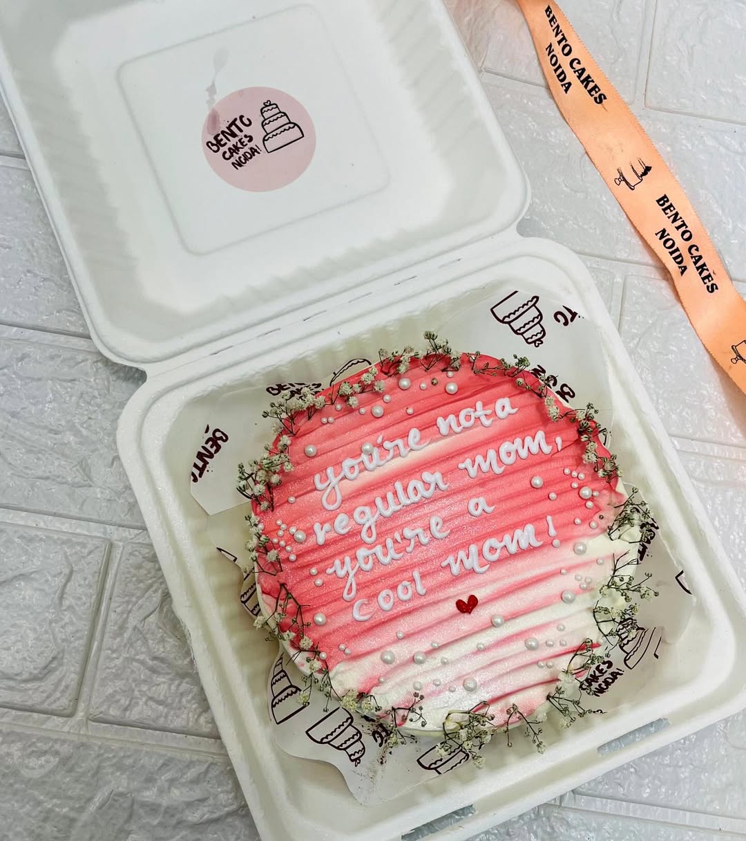 An aesthetic bento cake with white florals on side and a beautiful text written with white icing on it.