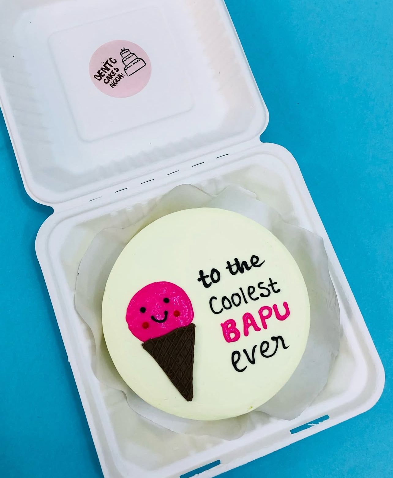 A beautifully decorated white cake featuring a pink ice cream cone illustration and the text "to the Coolest BAPU ever".