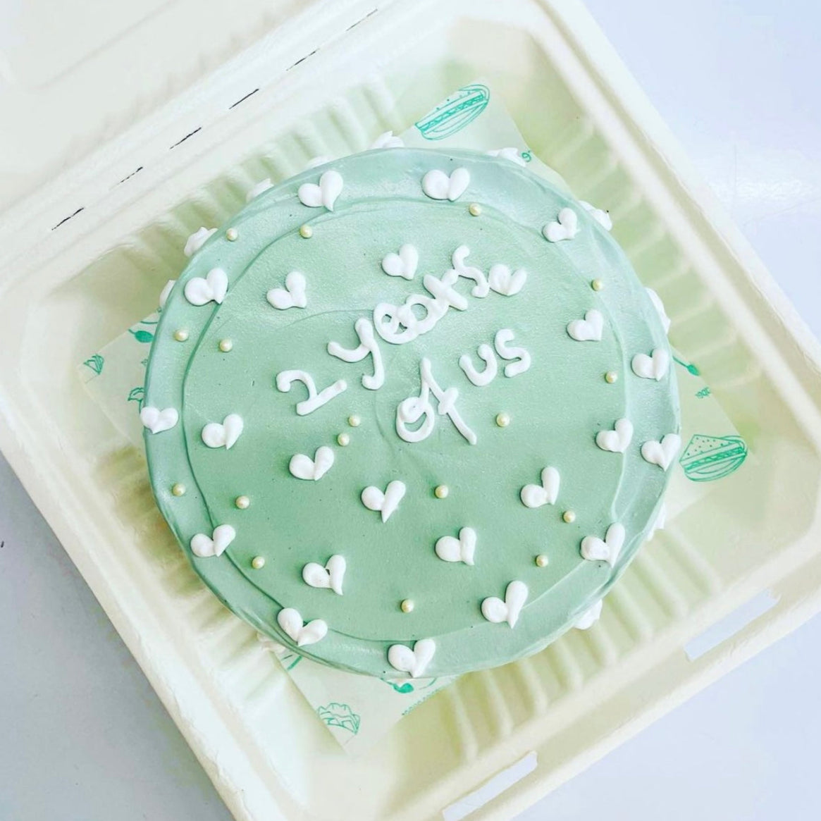 A celebratory cake in a soft foam container featuring the message "Happy 2 Years" elegantly written on top.