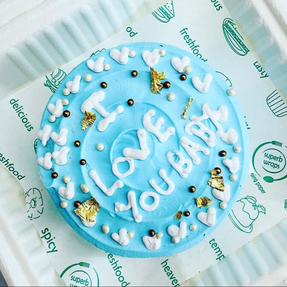 A blue cake in a plastic container, adorned with the words "Love You" written on top in elegant script.
