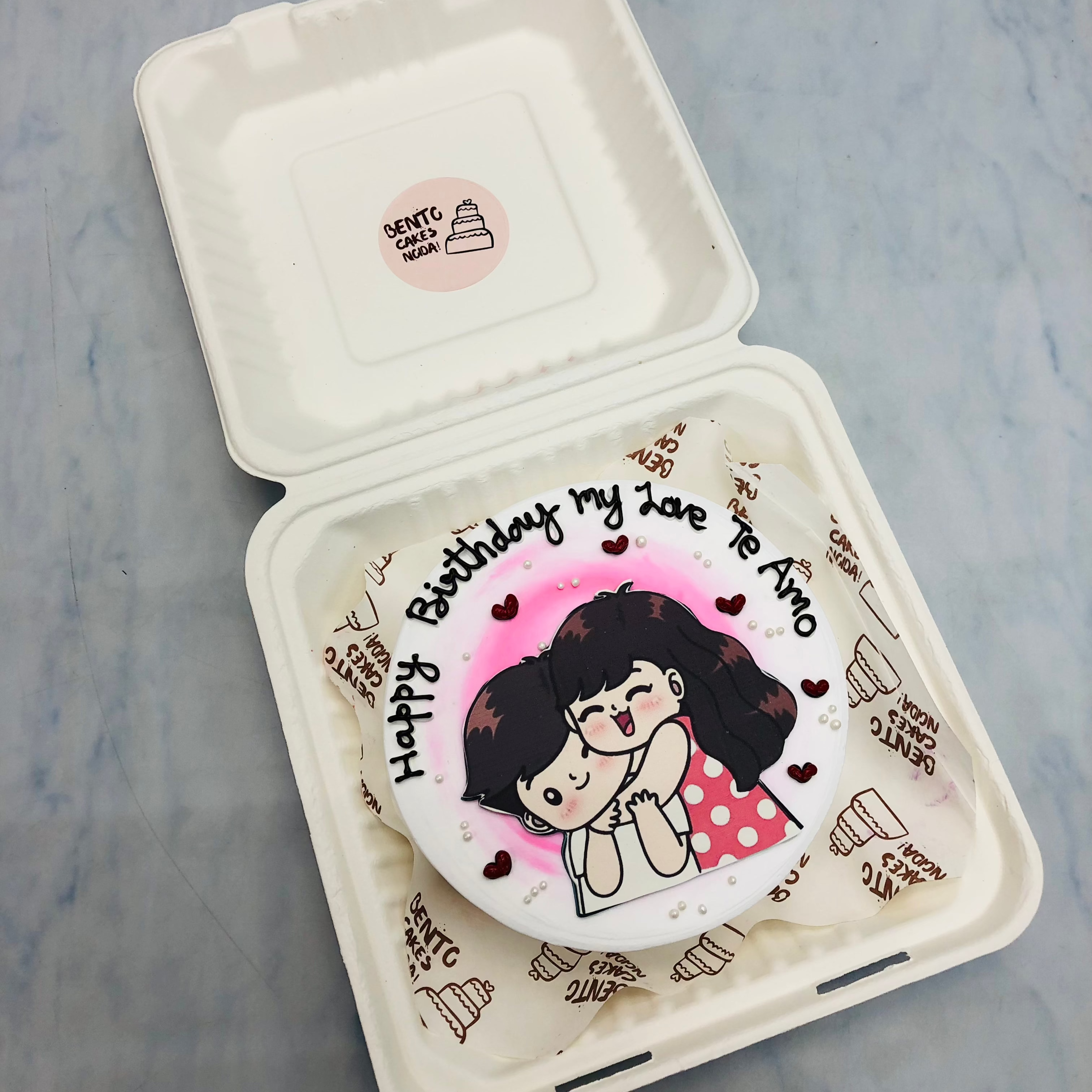 A beautifully decorated birthday cake featuring a couple embracing on top, symbolizing love and celebration.