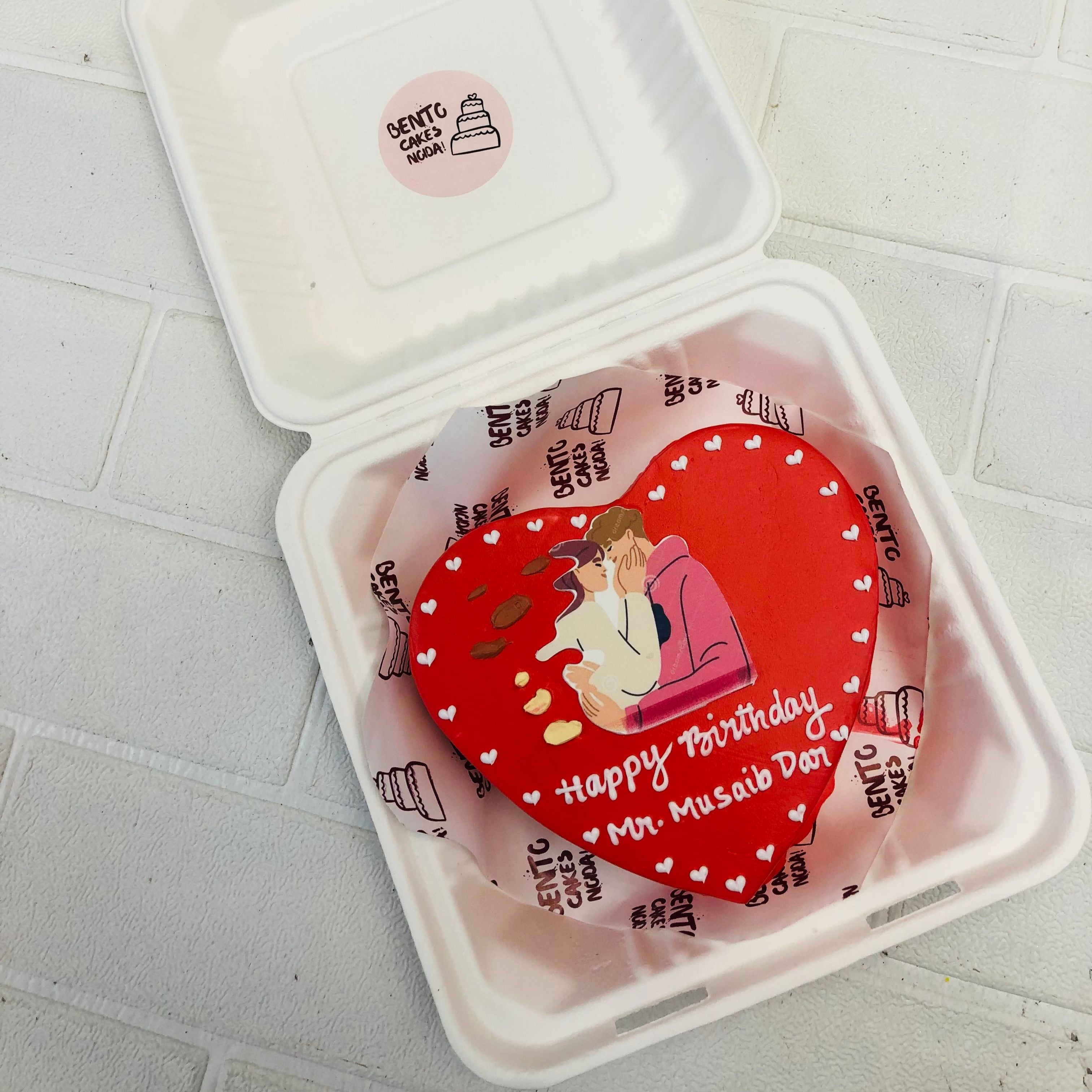 A dark red heart shape cake with little white hearts design and a sticker of loving couple placed on it.