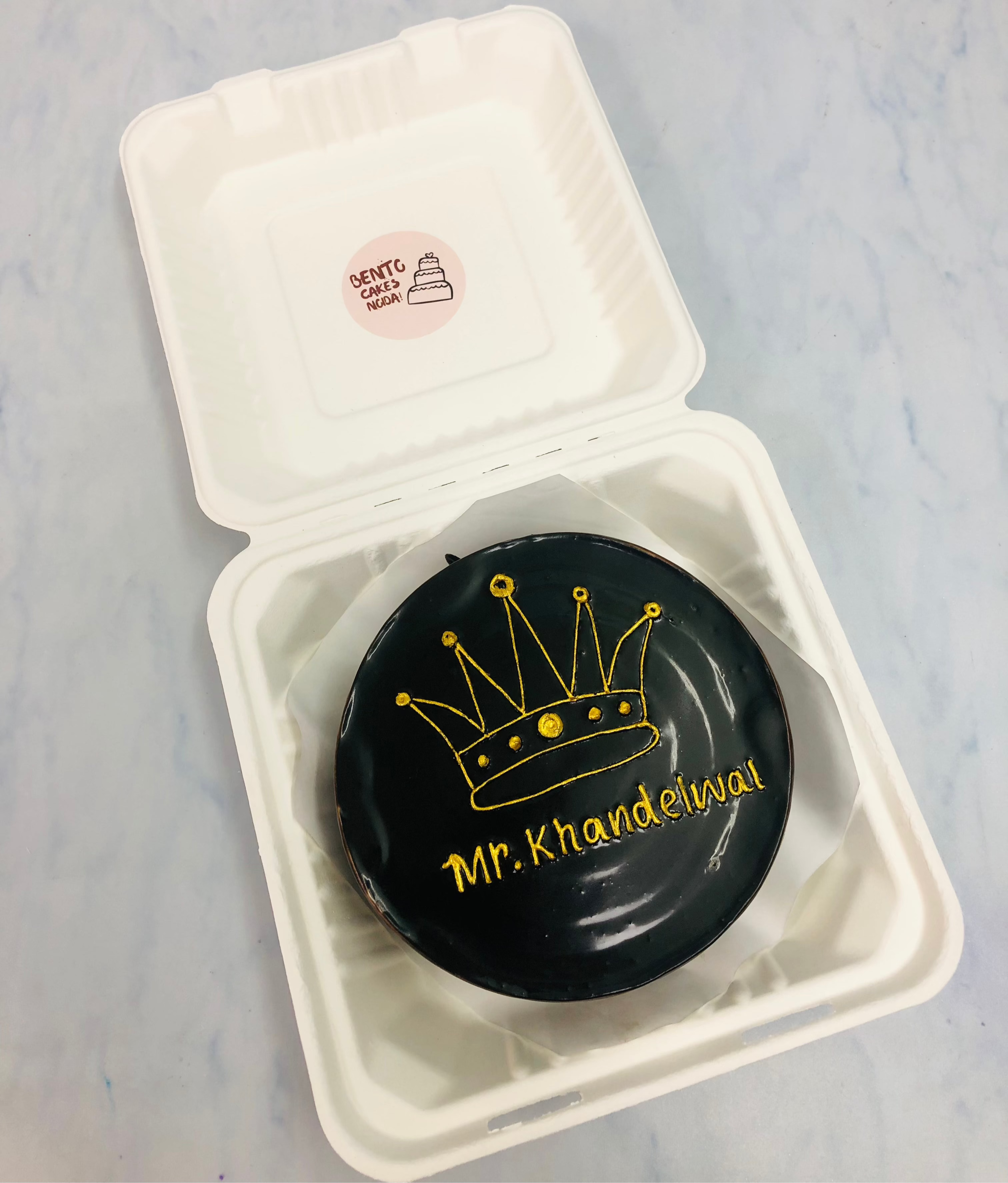 A chocolate bento cake is hesihned with golden crown design and a text "Mr. Khandelwal".