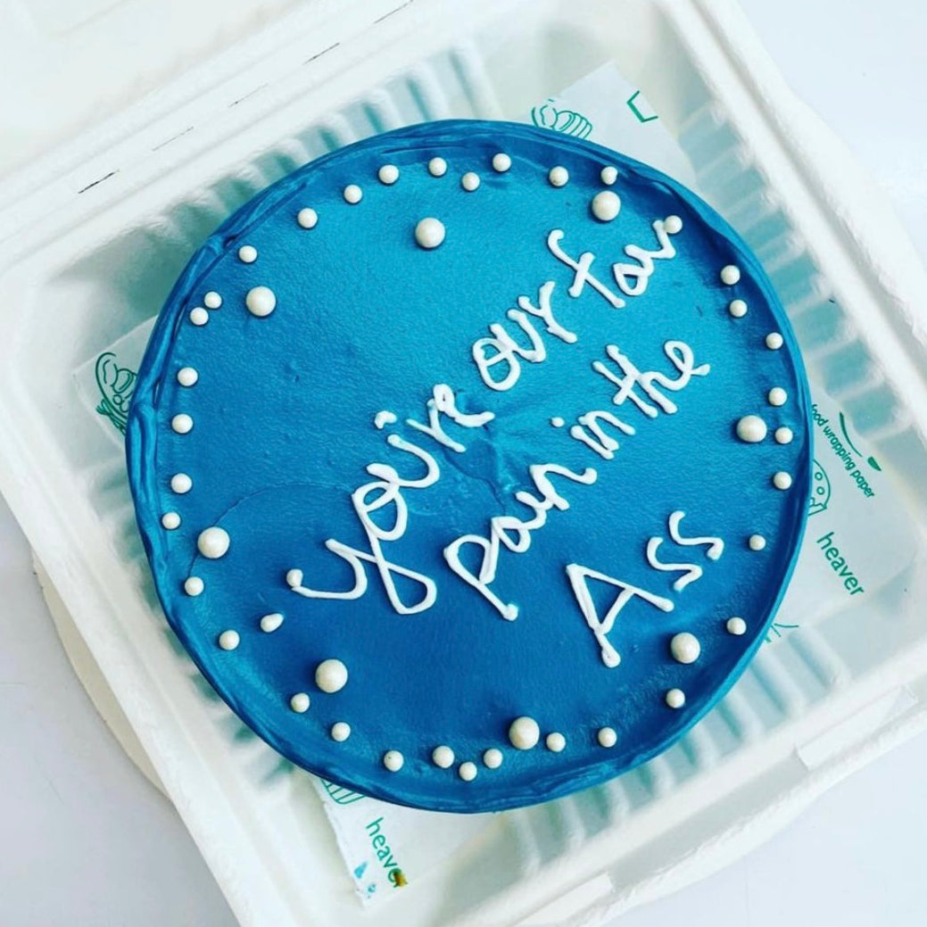 A cake displayed in a soft foam container, adorned with the words "You are our Fav. Pain in The Ass" in colorful icing.