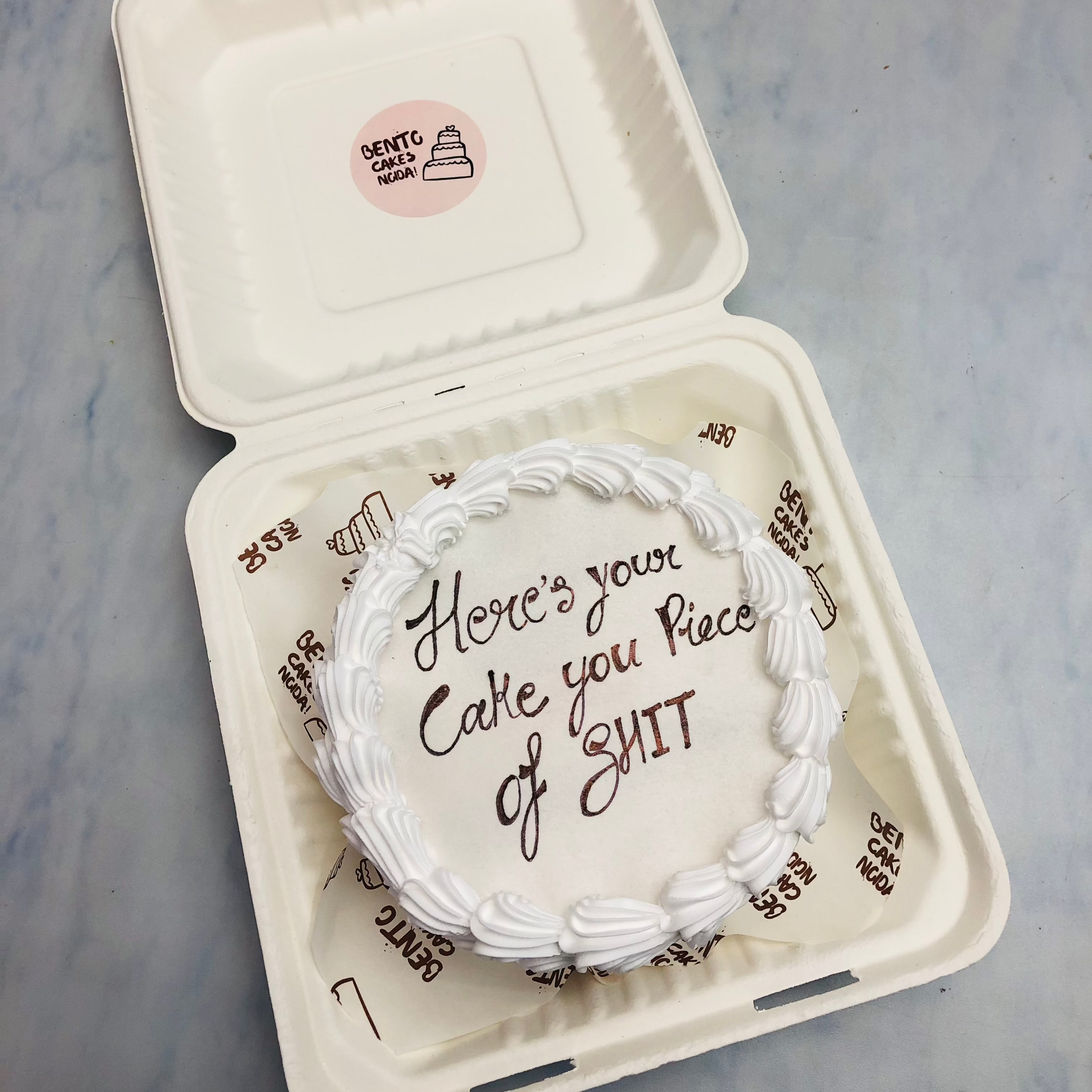 A romantic white cake featuring the playful message "Here's your Cake you Piece of SHIT" elegantly scripted on top.