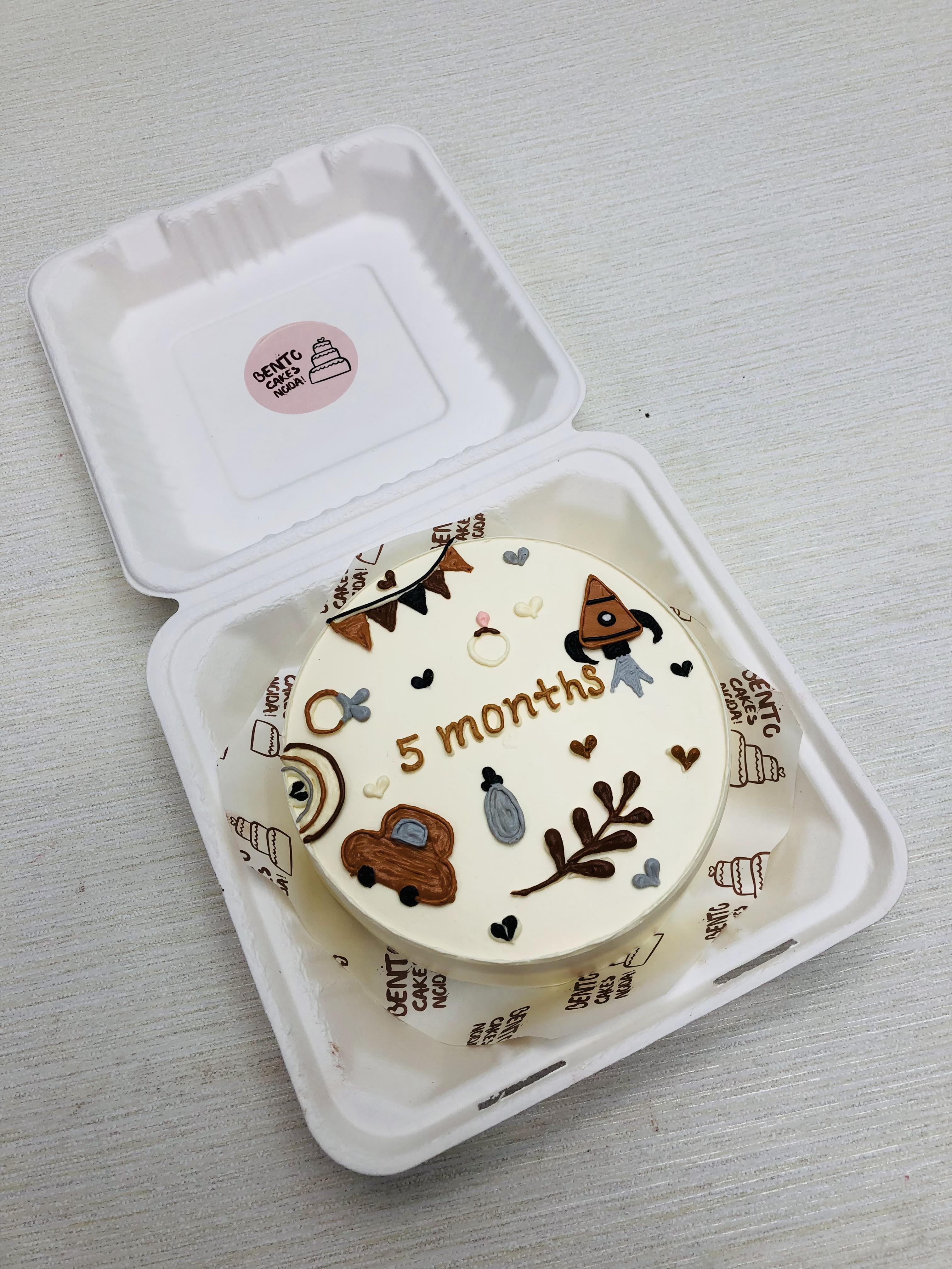 A white bento cake with 5 months baby beautiful toys designs in brown color.
