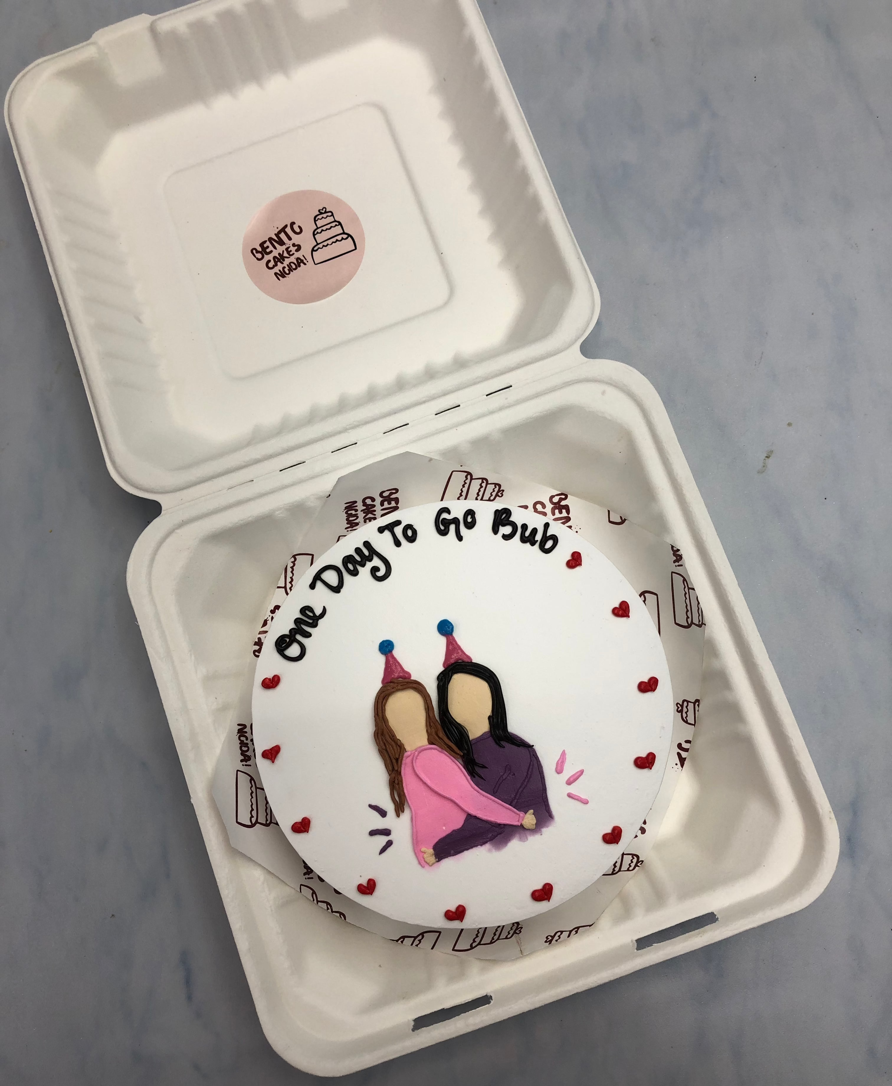 A white bento cake with two girl friends in hugging each other.