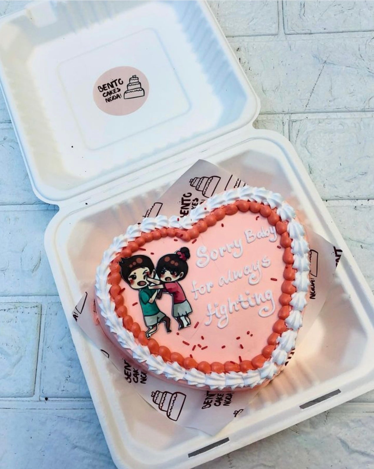 A peach color heart shape cake with a couple print on it and a sorry text on it.