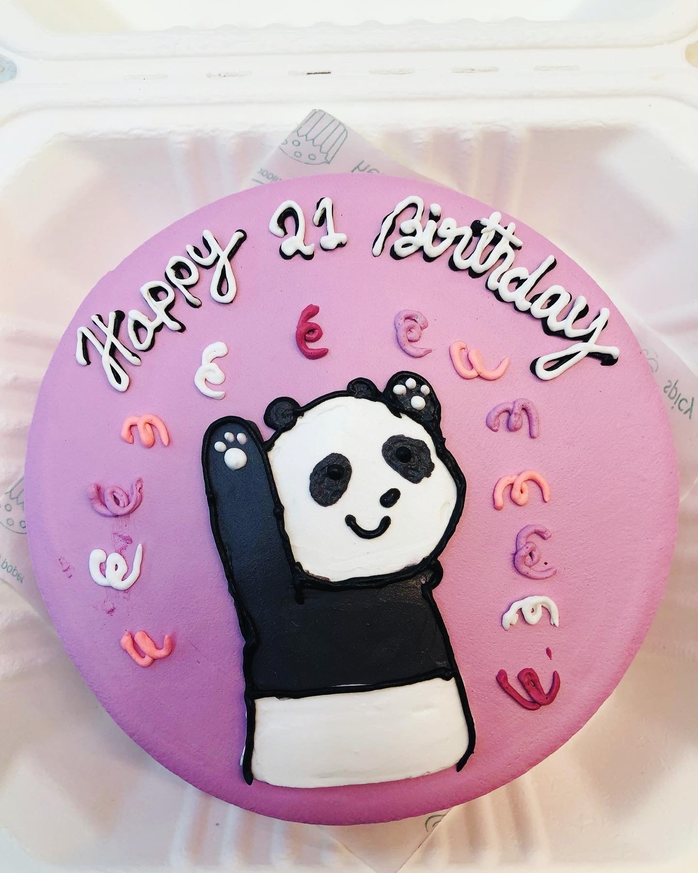 A purple cake decorated with a panda drawing and a text of "Happy 21 Birthday" written with black written icing.