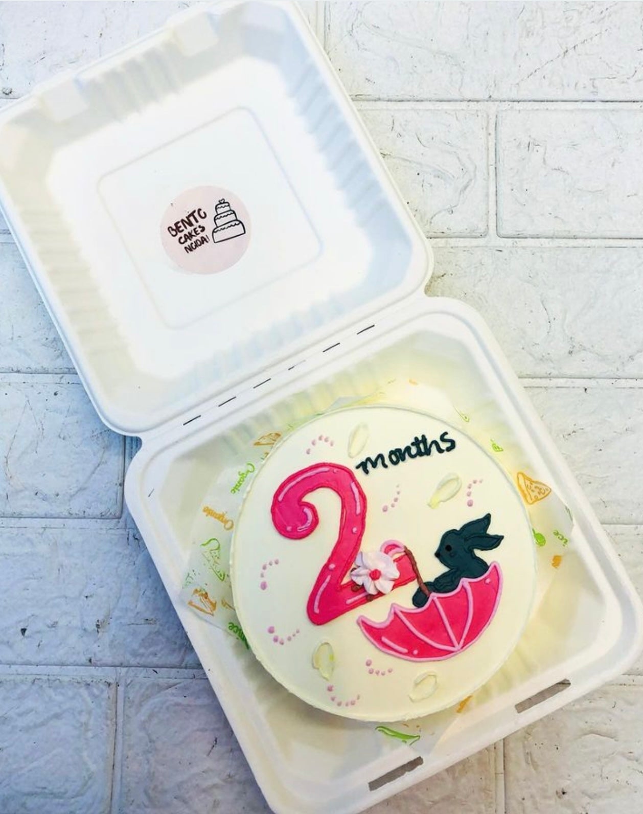 A white bento cake having umbrella design and a grey rabbit sleeping in it.