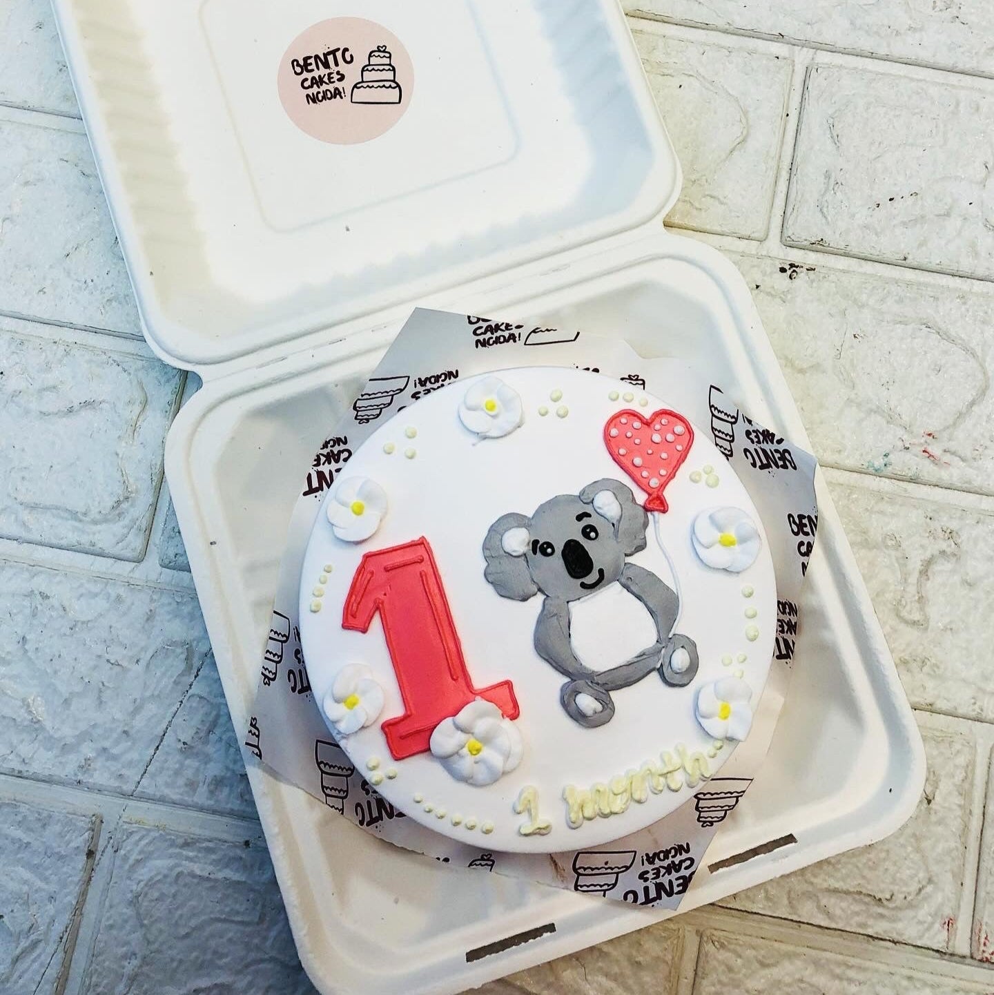 A white bento cake having a cute bear with balloon and number 1.