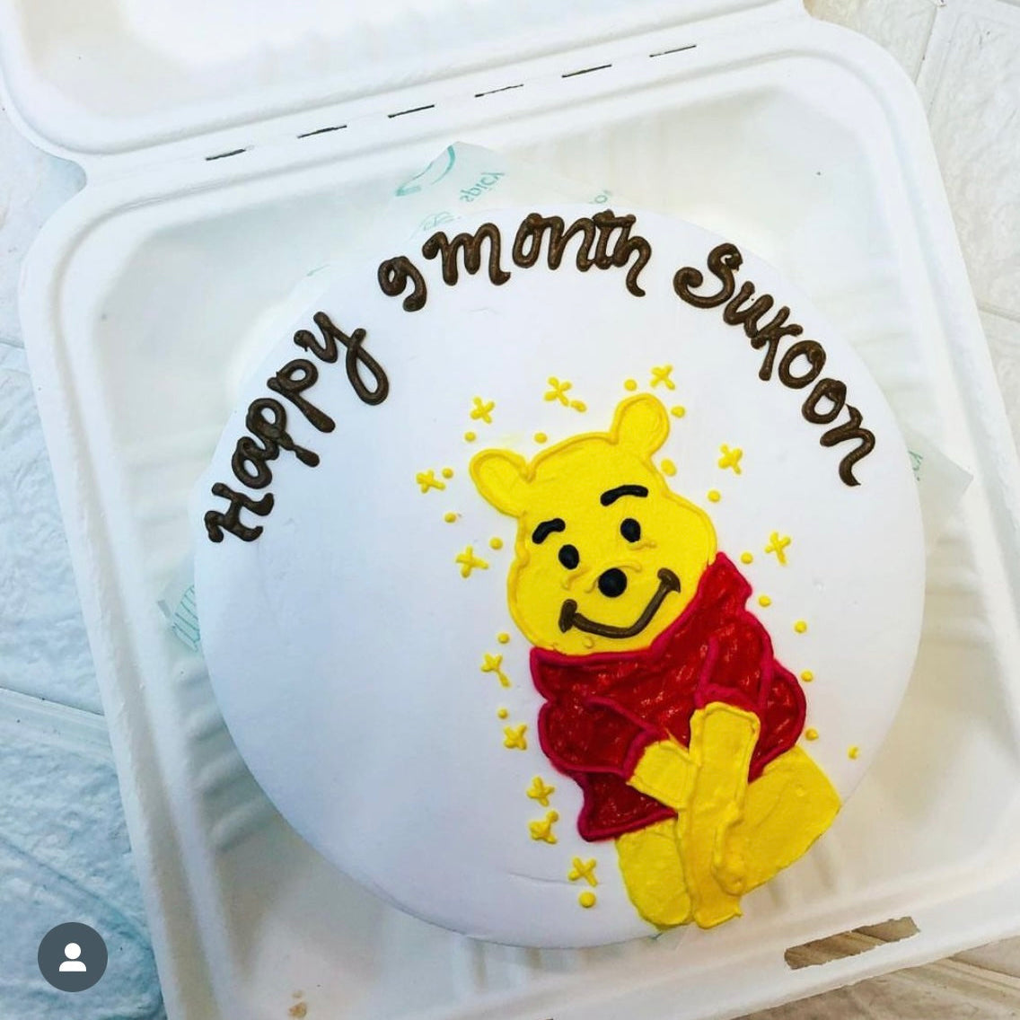 A white bento cake with a cute yellow bear design and a "Happy 9 months Sukoon" written above the bear design.