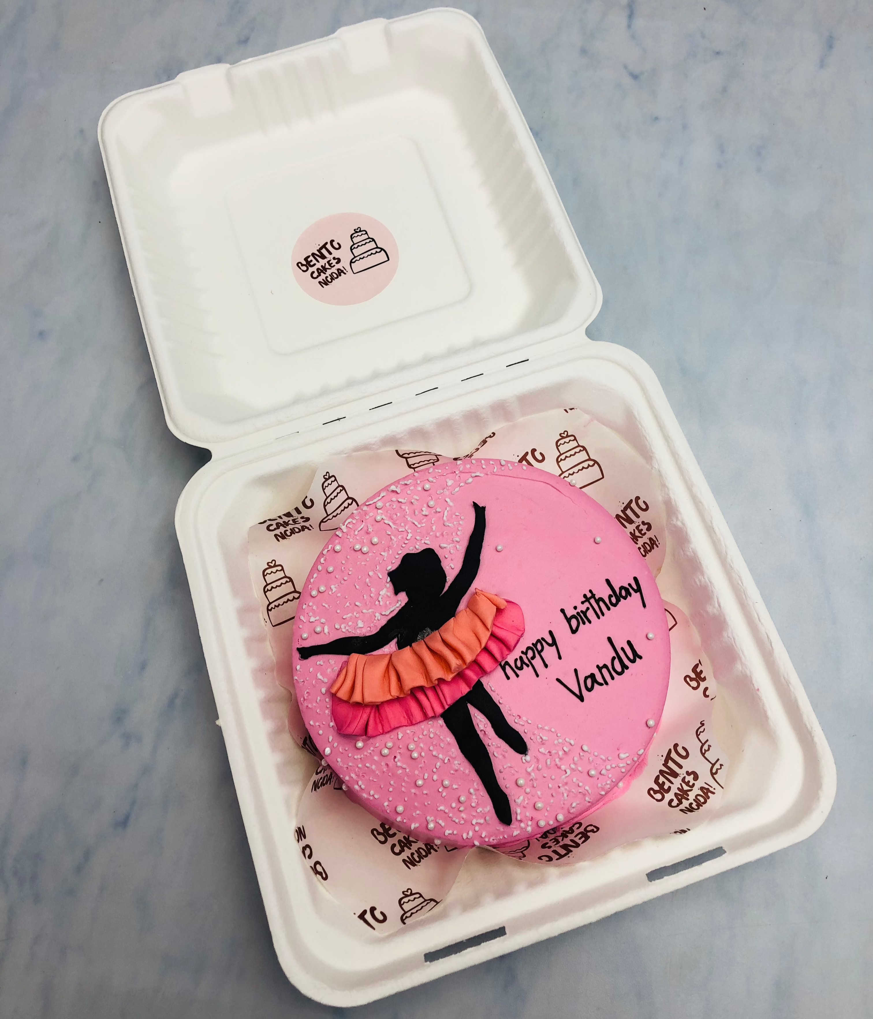 A pink frosting bento cake having a fondant girl design wearing pink-orange skirt on her birthday.