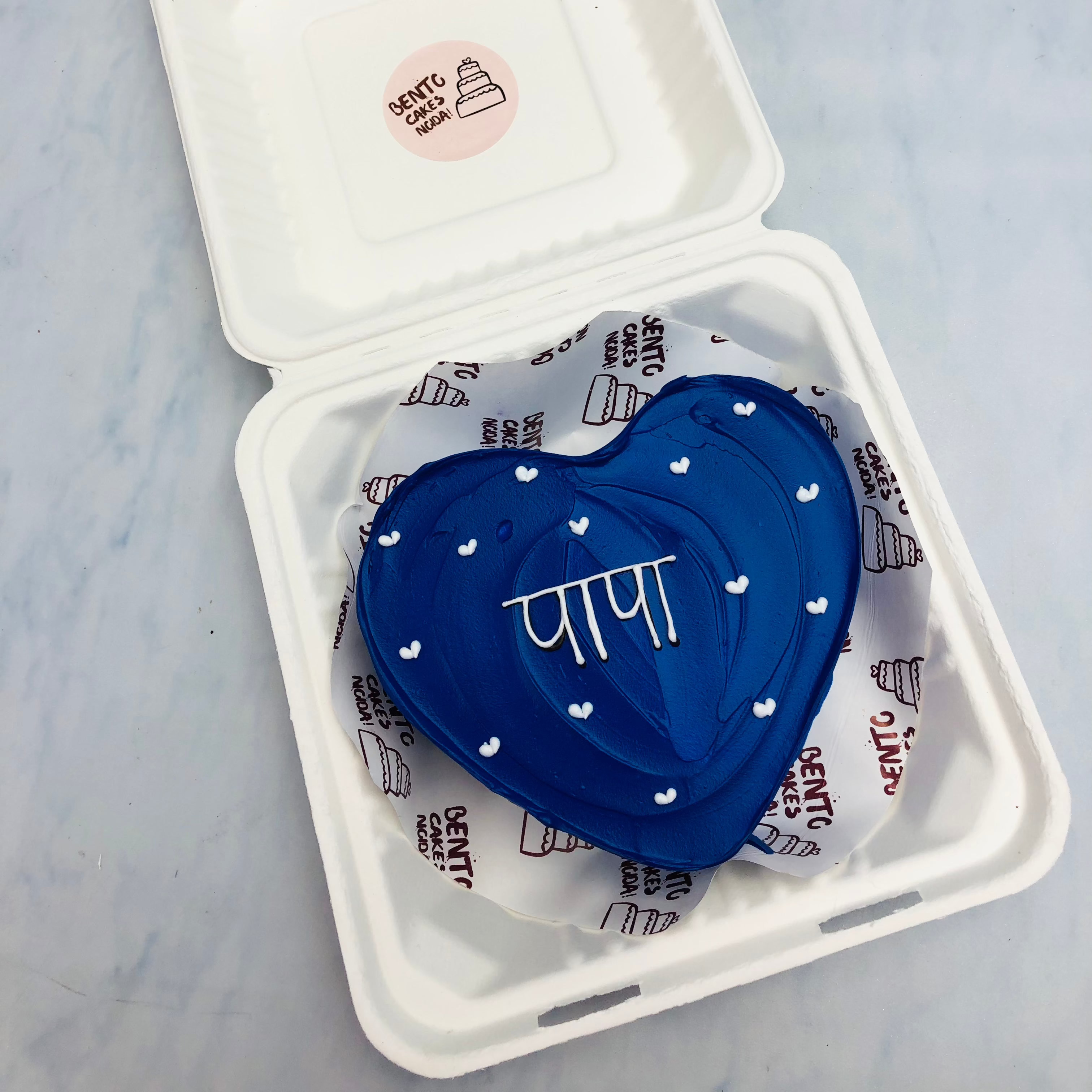 A dark blue hearts shape cake with wavy design and a text written with white color on it.